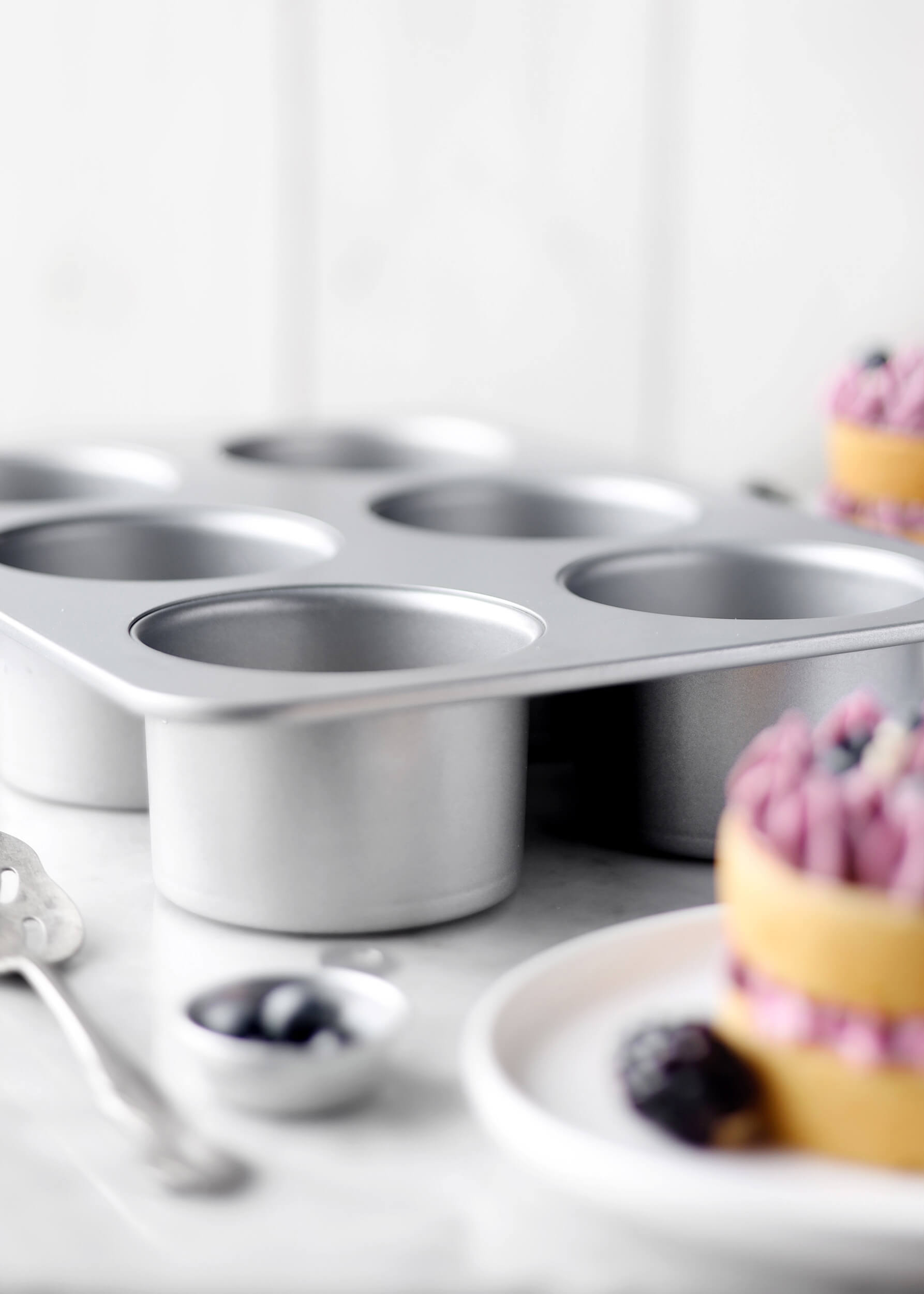 Forma do muffinek z małymi ciastkami, jagodami i łyżką.