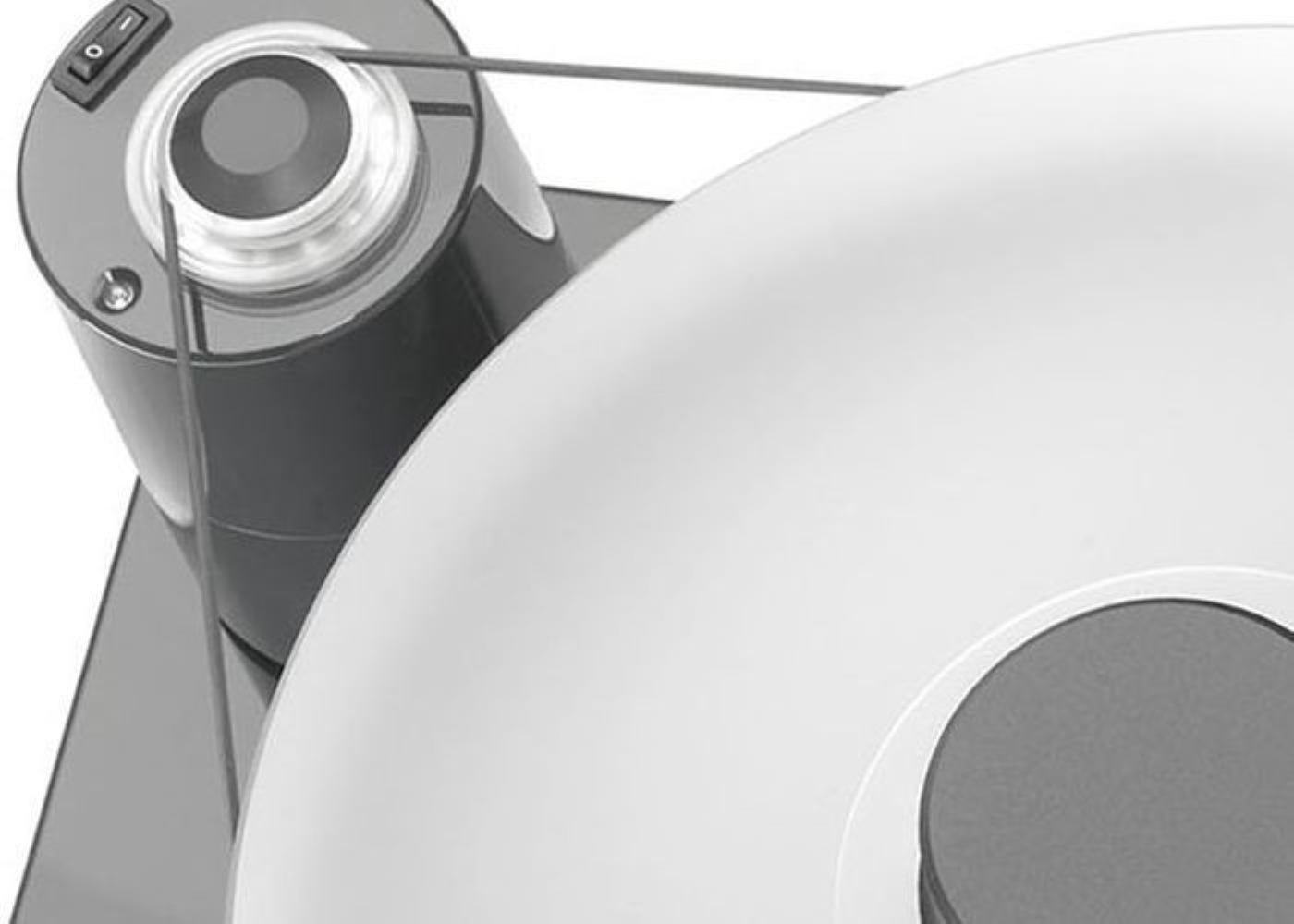 Zbliżenie urządzenia z szarą obudową, przełącznikiem i paskiem owijającym się wokół białego dysku.