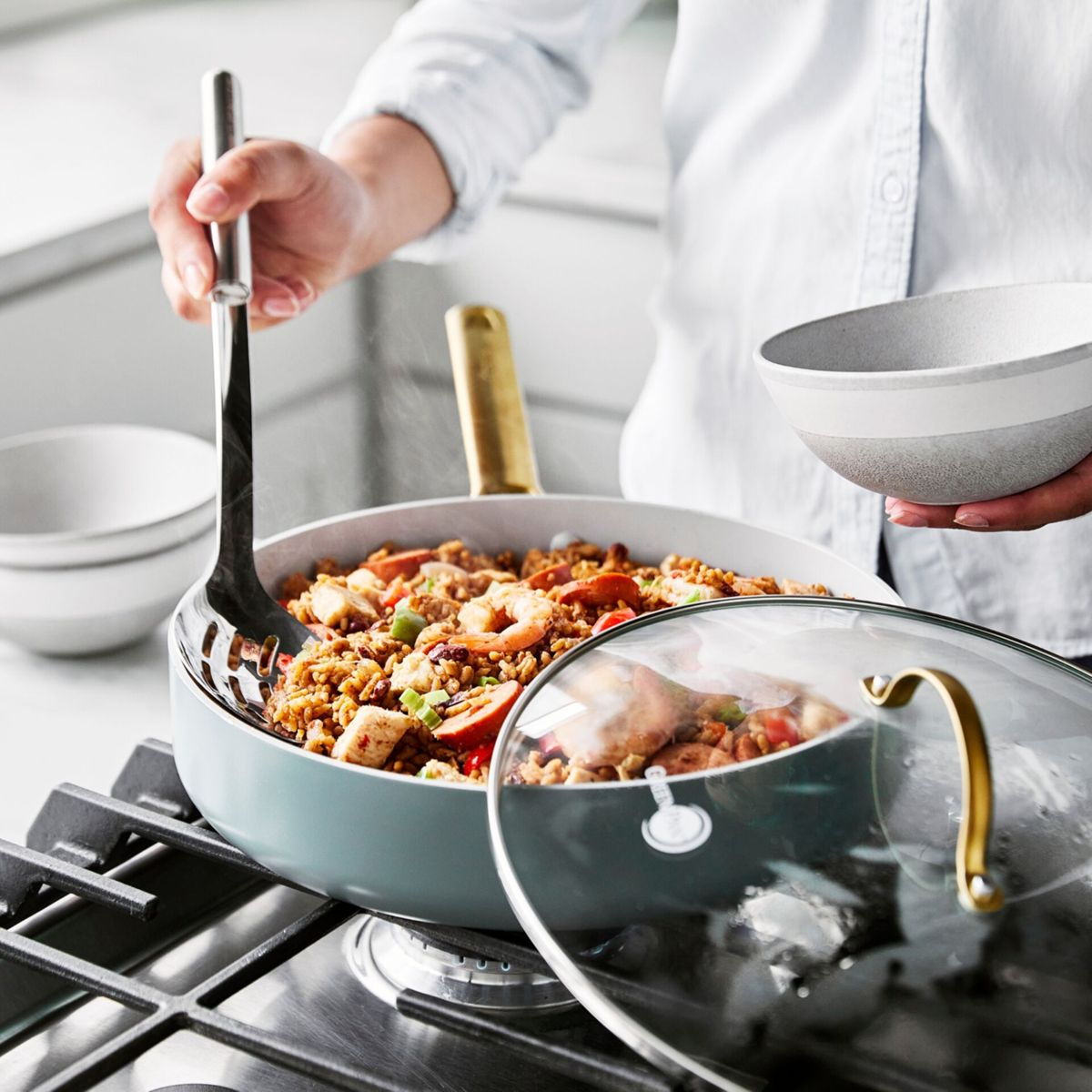 Eine Person rührt in einer Pfanne mit Paella, garniert mit Garnelen und Hähnchen.