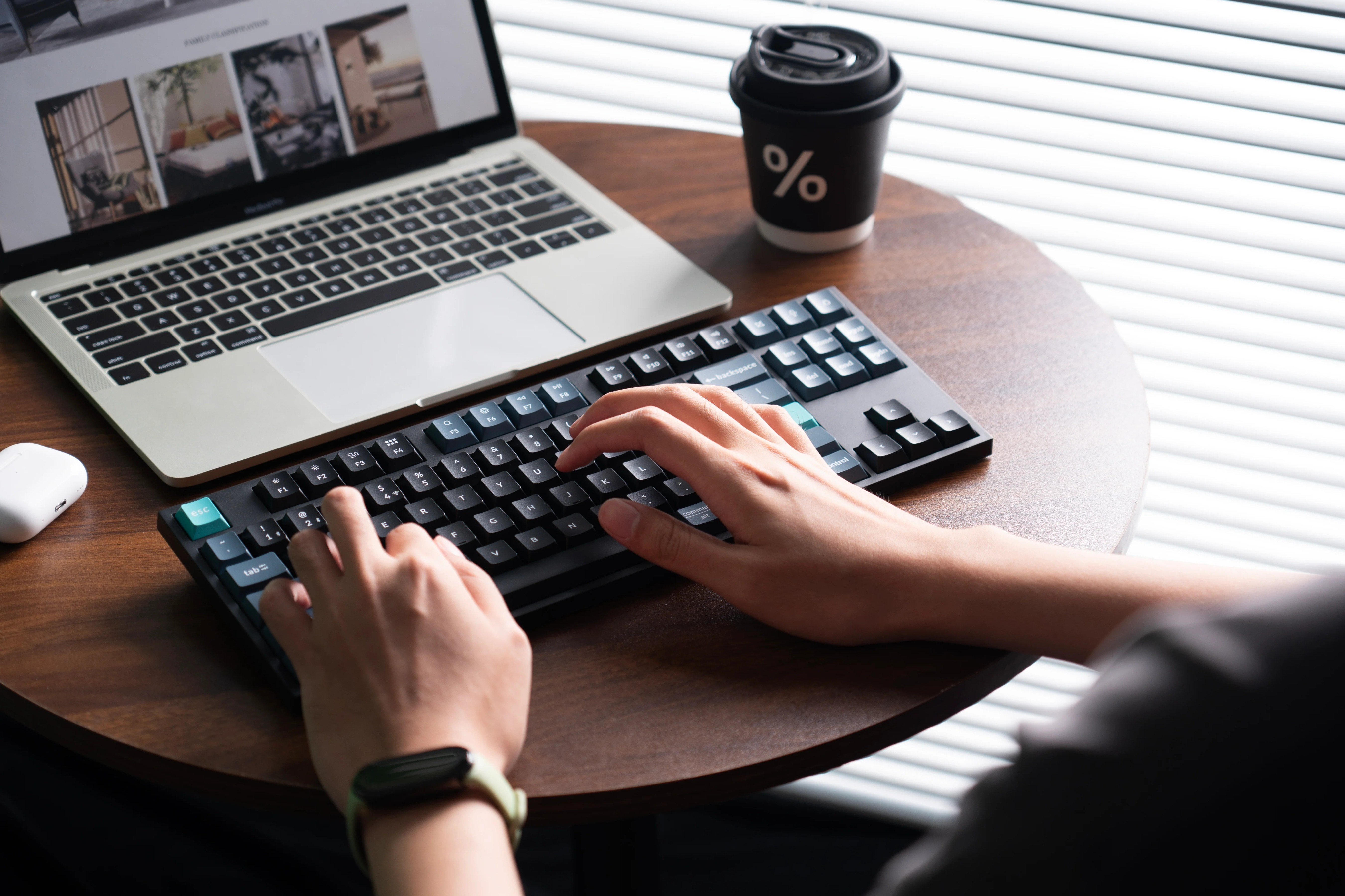 Dłonie piszące na klawiaturze obok laptopa i kubka z kawą.