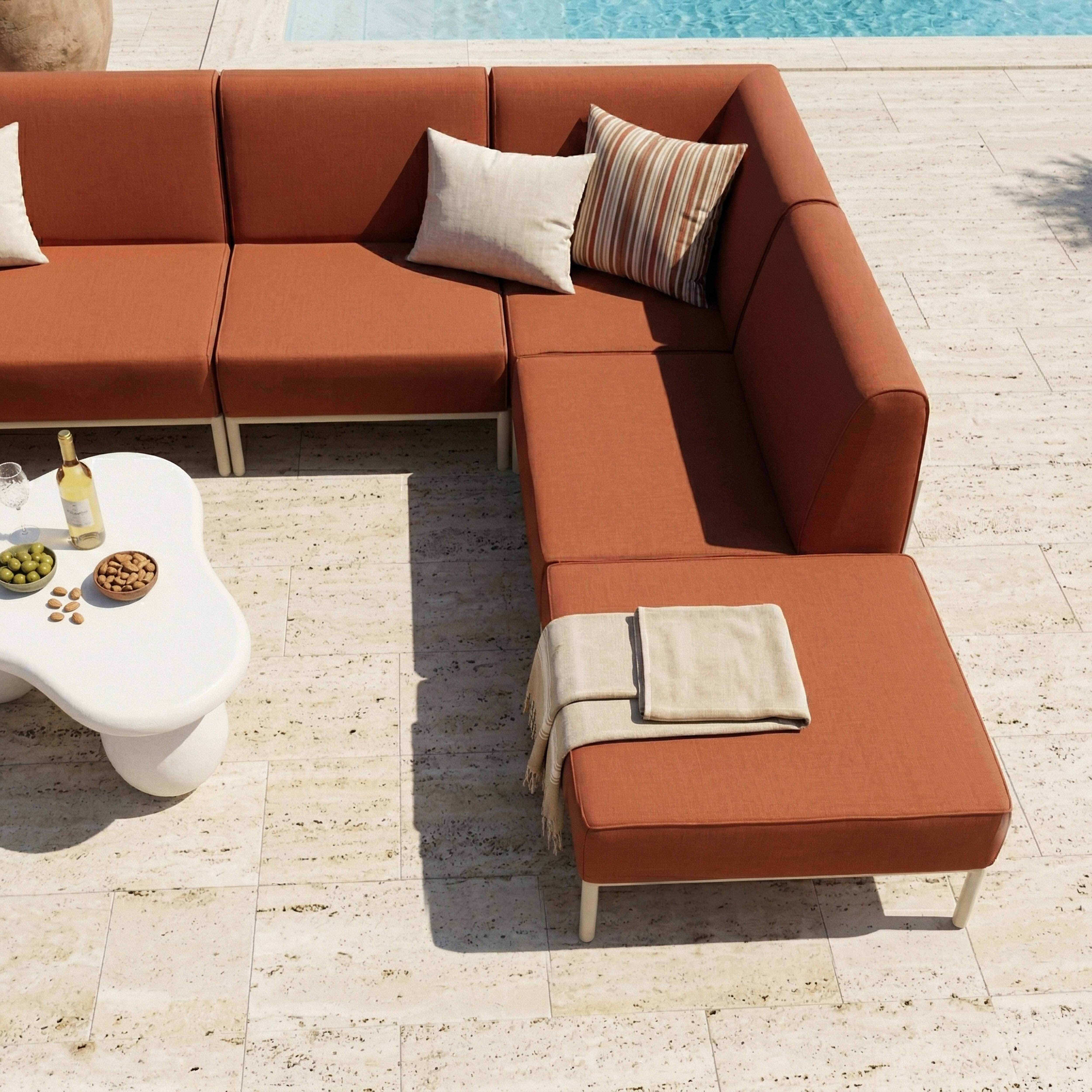 Orange Couch am Pool mit weißem Tisch, Wein und Snacks.