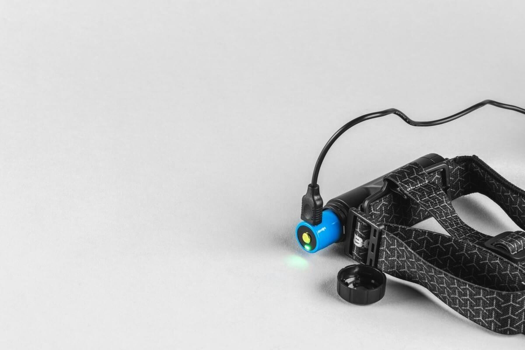 Boîtier de lampe frontale bleu avec cordon noir, brillant sur fond gris.
