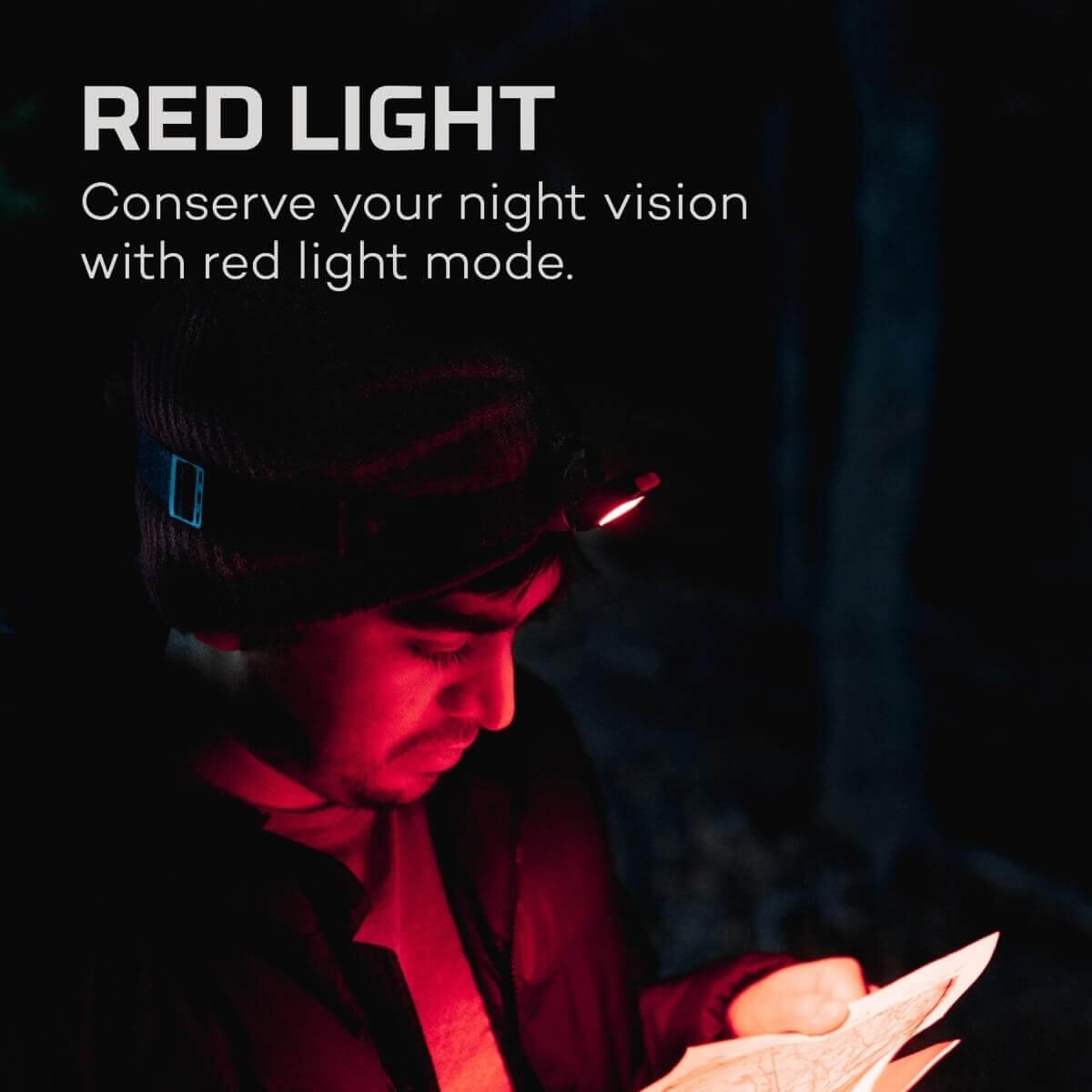 Homme avec lampe frontale lit une carte à la lumière rouge.