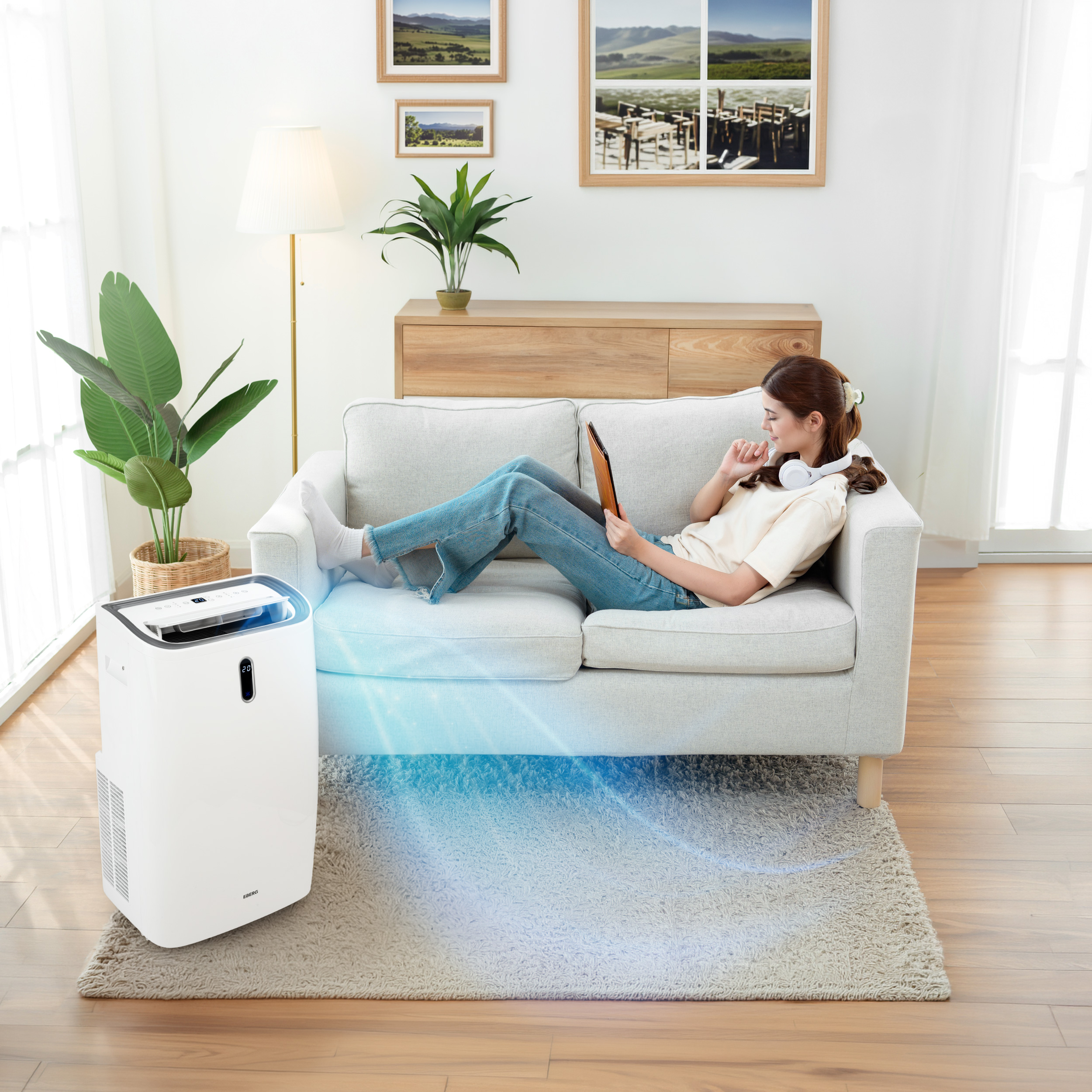 Kobieta leży na kanapie, używając tabletu. Przed nią stoi biały klimatyzator.