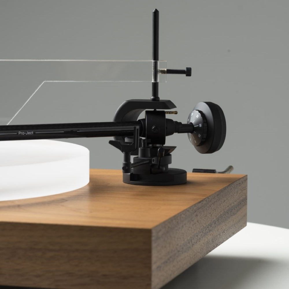 Czarny metalowy ramie gramofonu z pokrętłem siedzi na drewnianej podstawie.