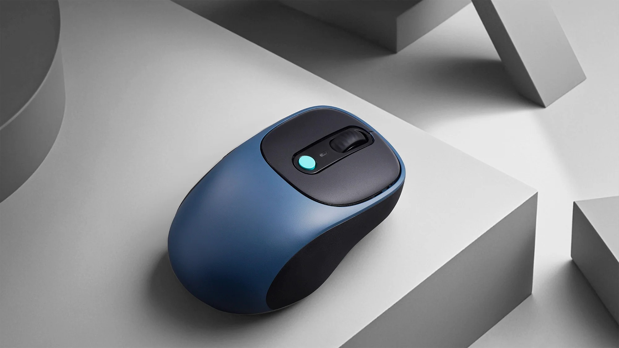 Niebieska mysz komputerowa z kółkiem i niebieskim przyciskiem leży na szarych blokach.