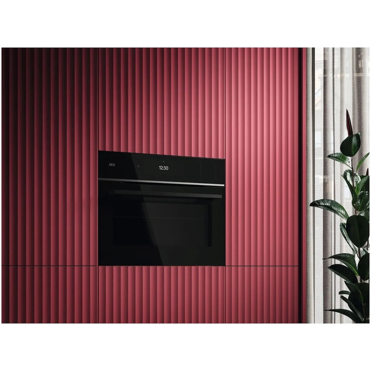 Built-in oven in a red, vertically ribbed kitchen cabinet, next to a window with curtains and a plant.