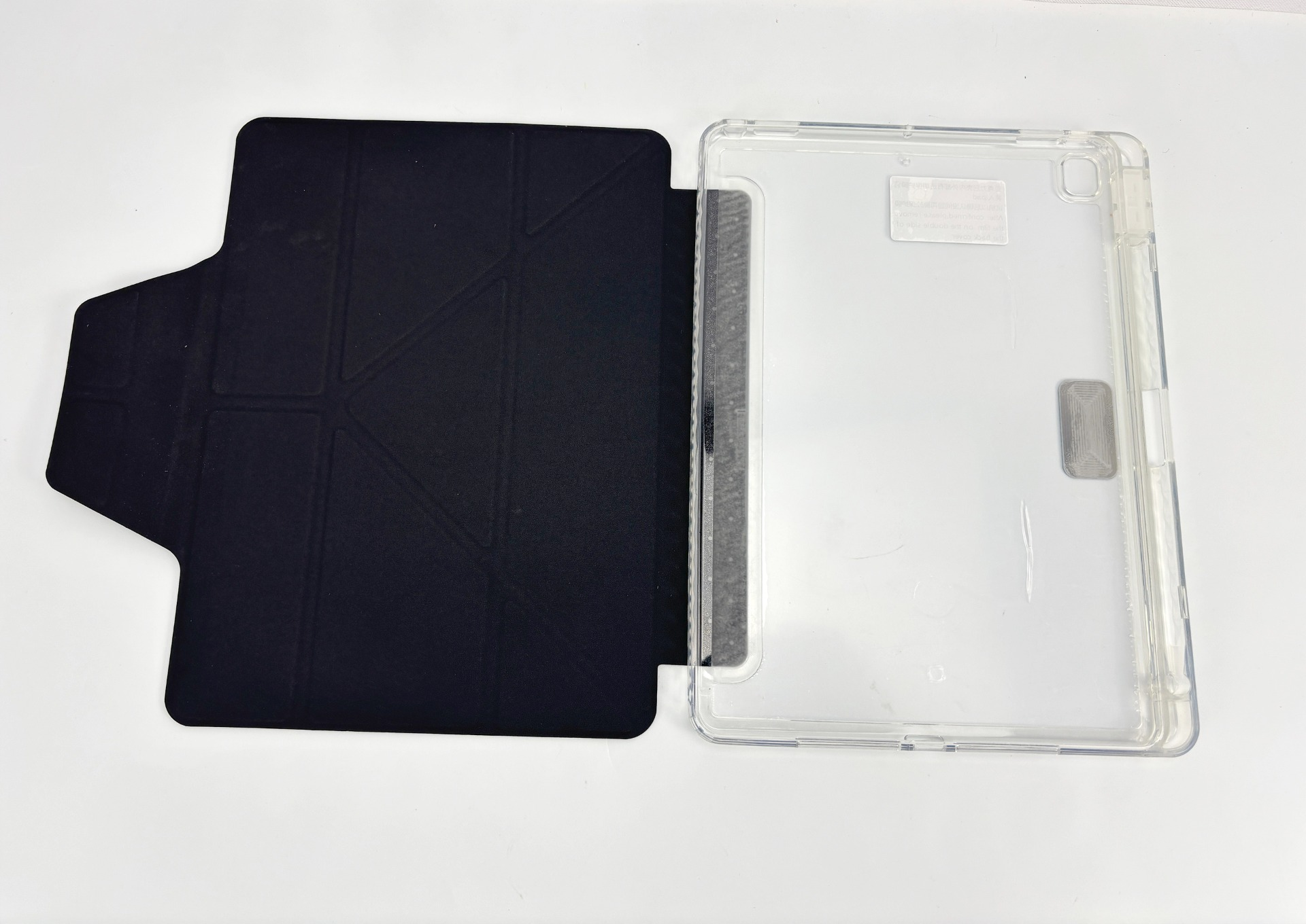 Eine schwarze Tablet-Hülle liegt offen neben einer durchsichtigen Plastikhülle auf weißem Untergrund.