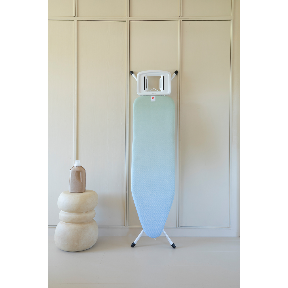 A gradient ironing board stands next to a side table with a bottle.