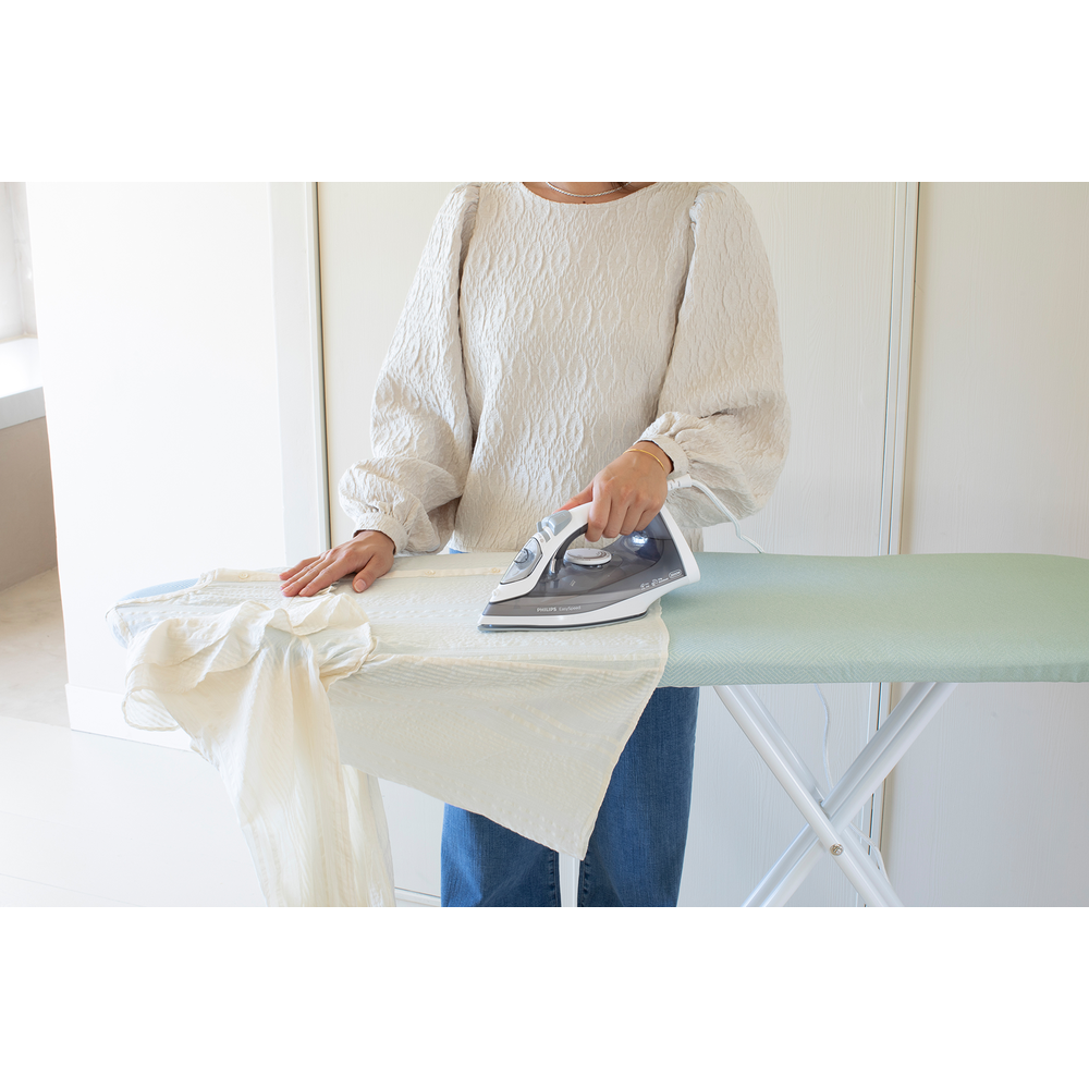 A person irons a light-colored shirt on an ironing board.