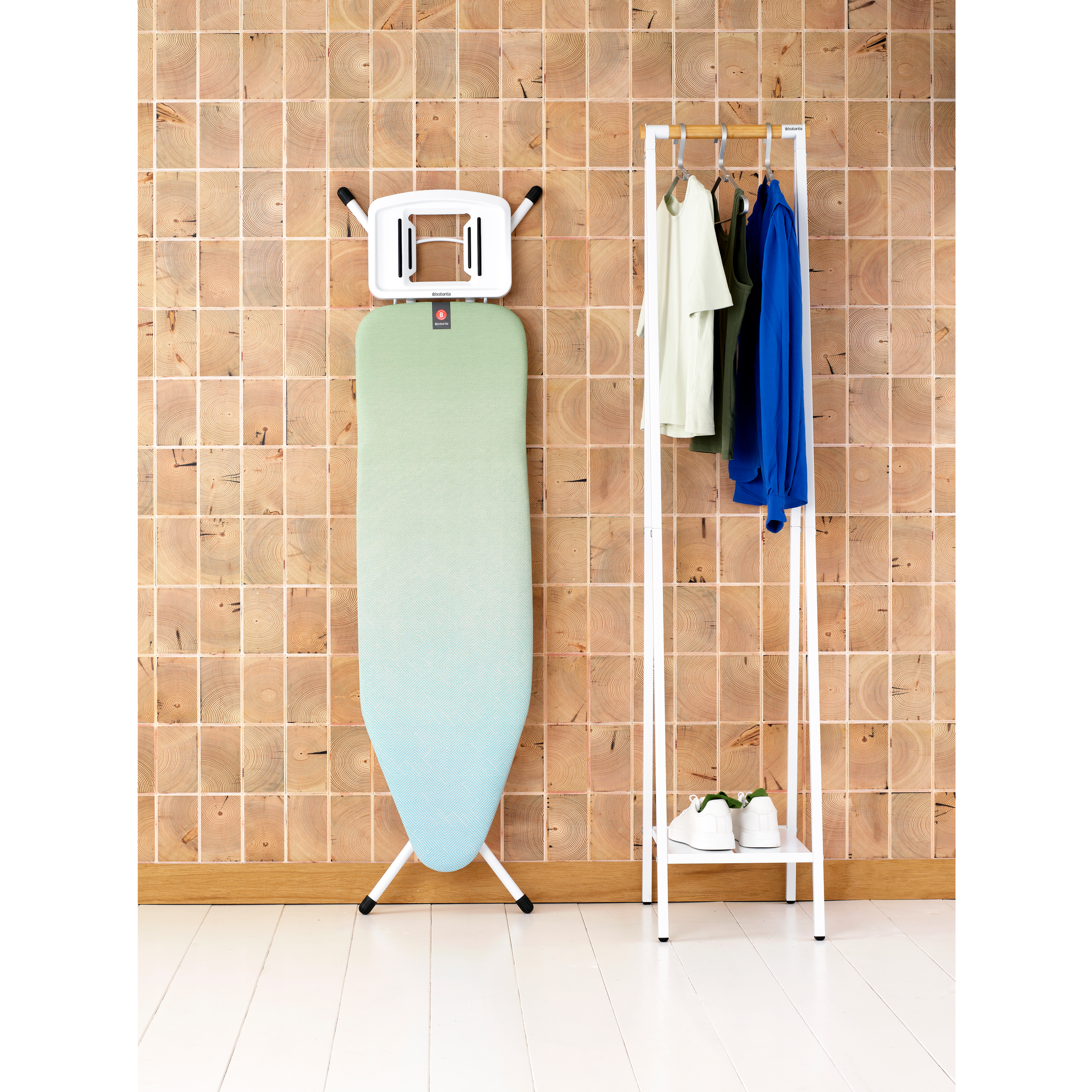 Ironing board on a stand against wood wall with clothes and shoes.