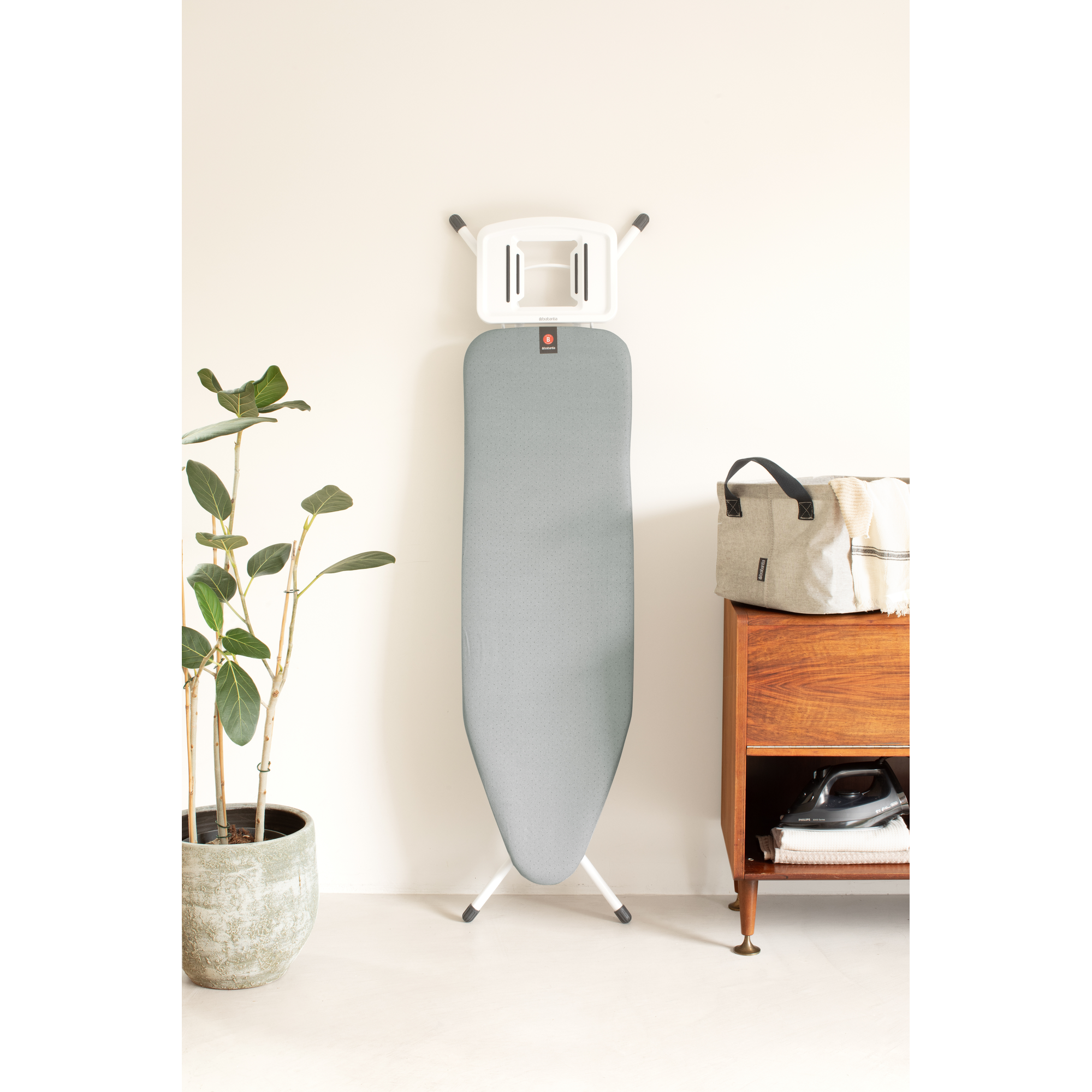 Une planche à repasser à côté d'une armoire en bois avec fer et panier.