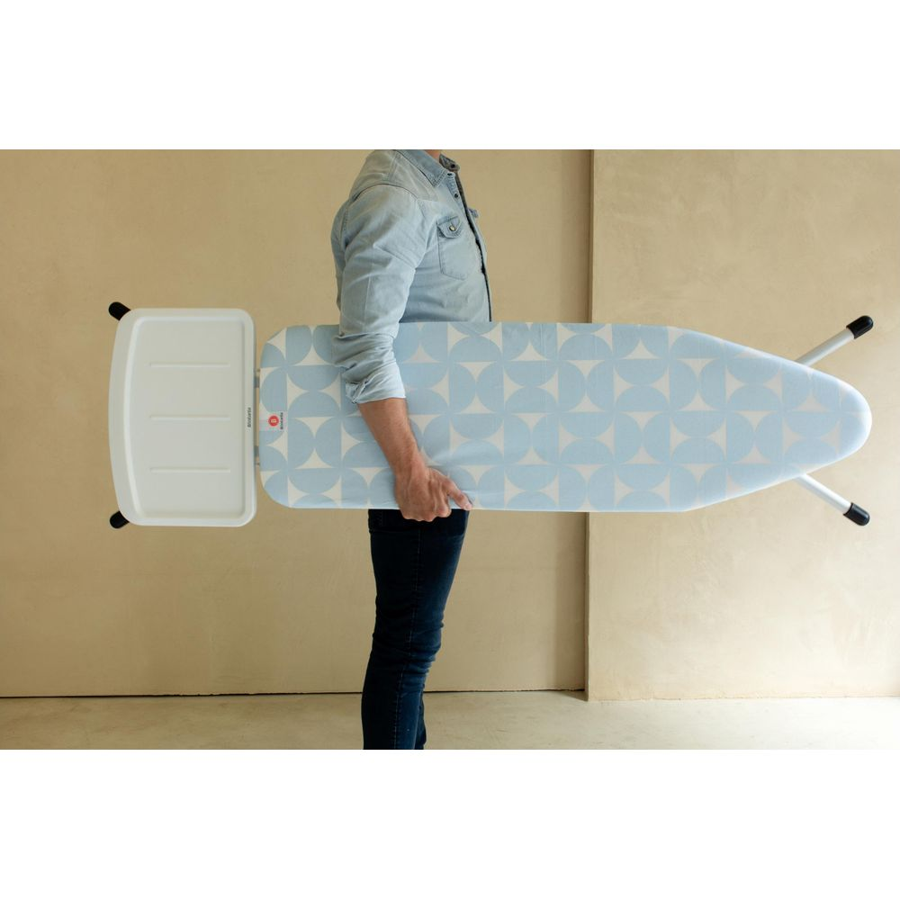 Man holding a blue ironing board with geometric pattern and white accessory.