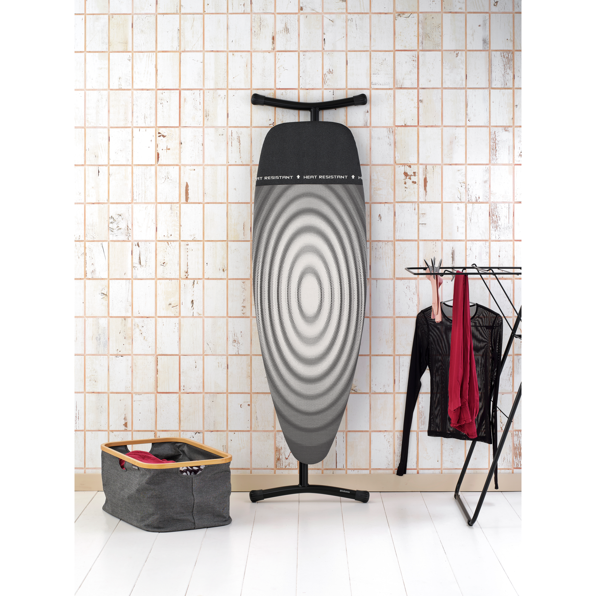 Une planche à repasser à motifs se trouve à côté d'un étendoir à linge avec des vêtements et un panier à linge.