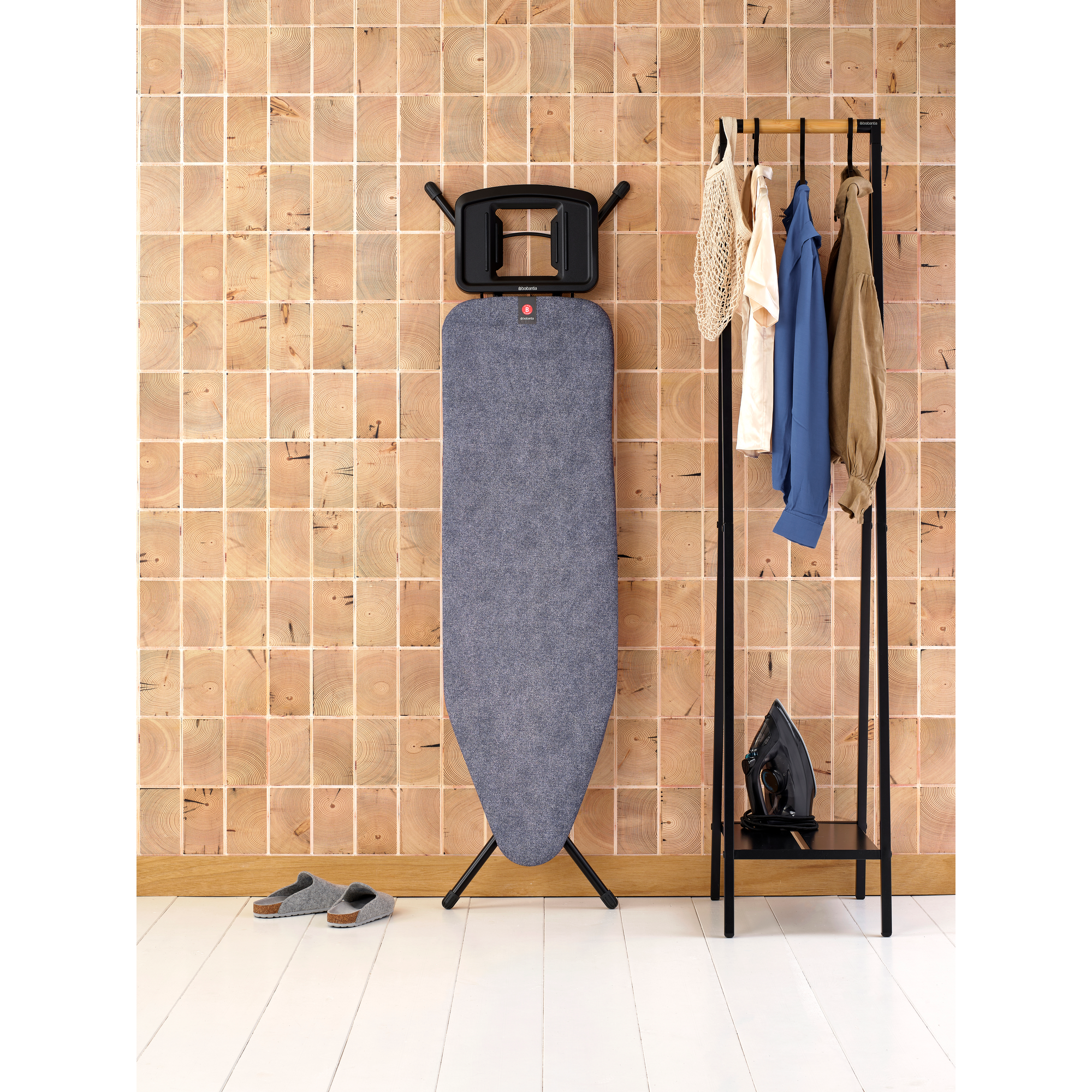 Iron, clothes rack with clothes, ironing board and slippers against wood wall.