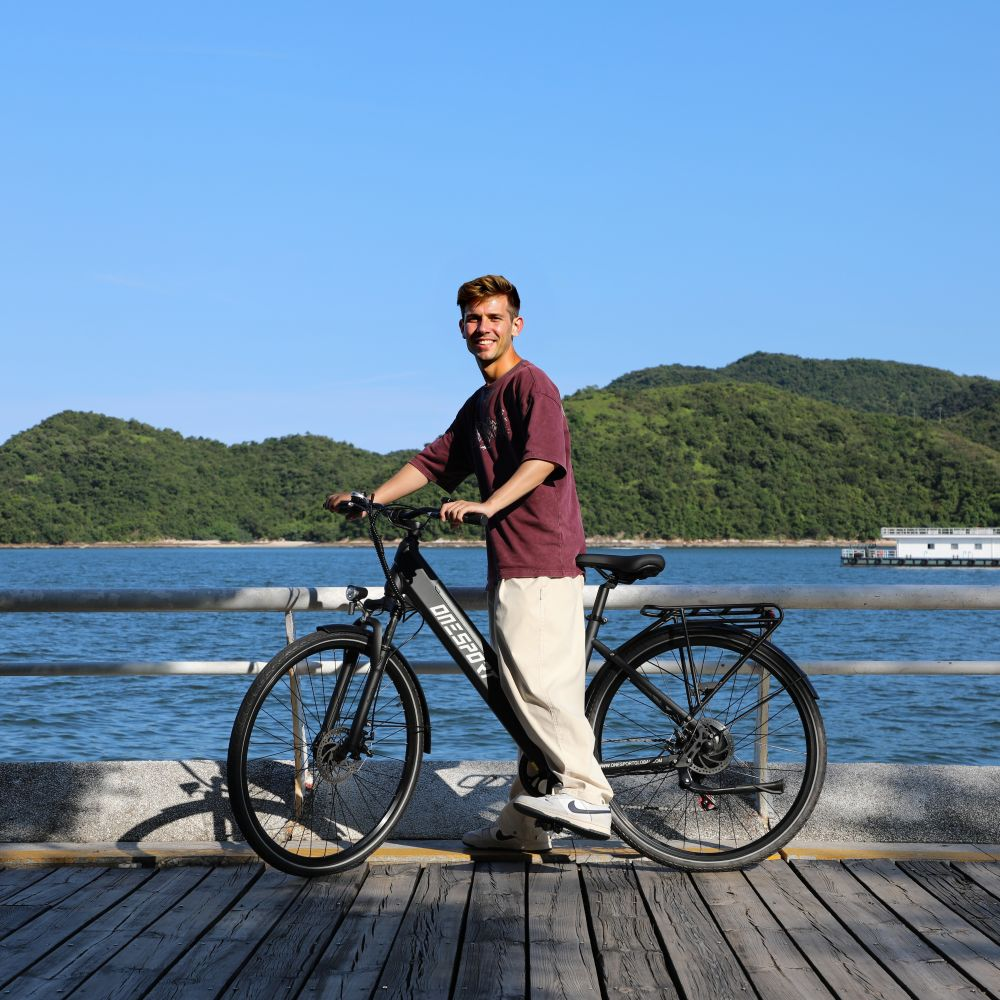 Un uomo con una bicicletta si trova su un molo di legno vicino all'acqua con colline verdi.