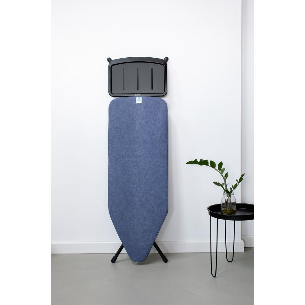 Blue ironing board against a white wall, with a black attachment and small table nearby.
