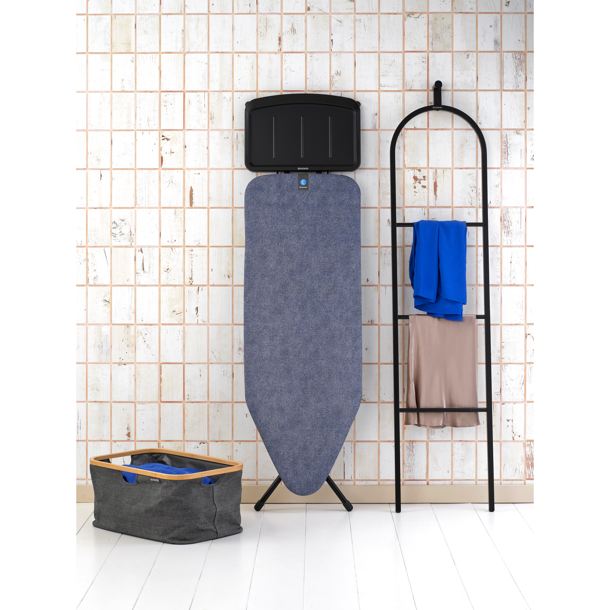 A blue ironing board stands next to a towel rack with blue and beige towels.