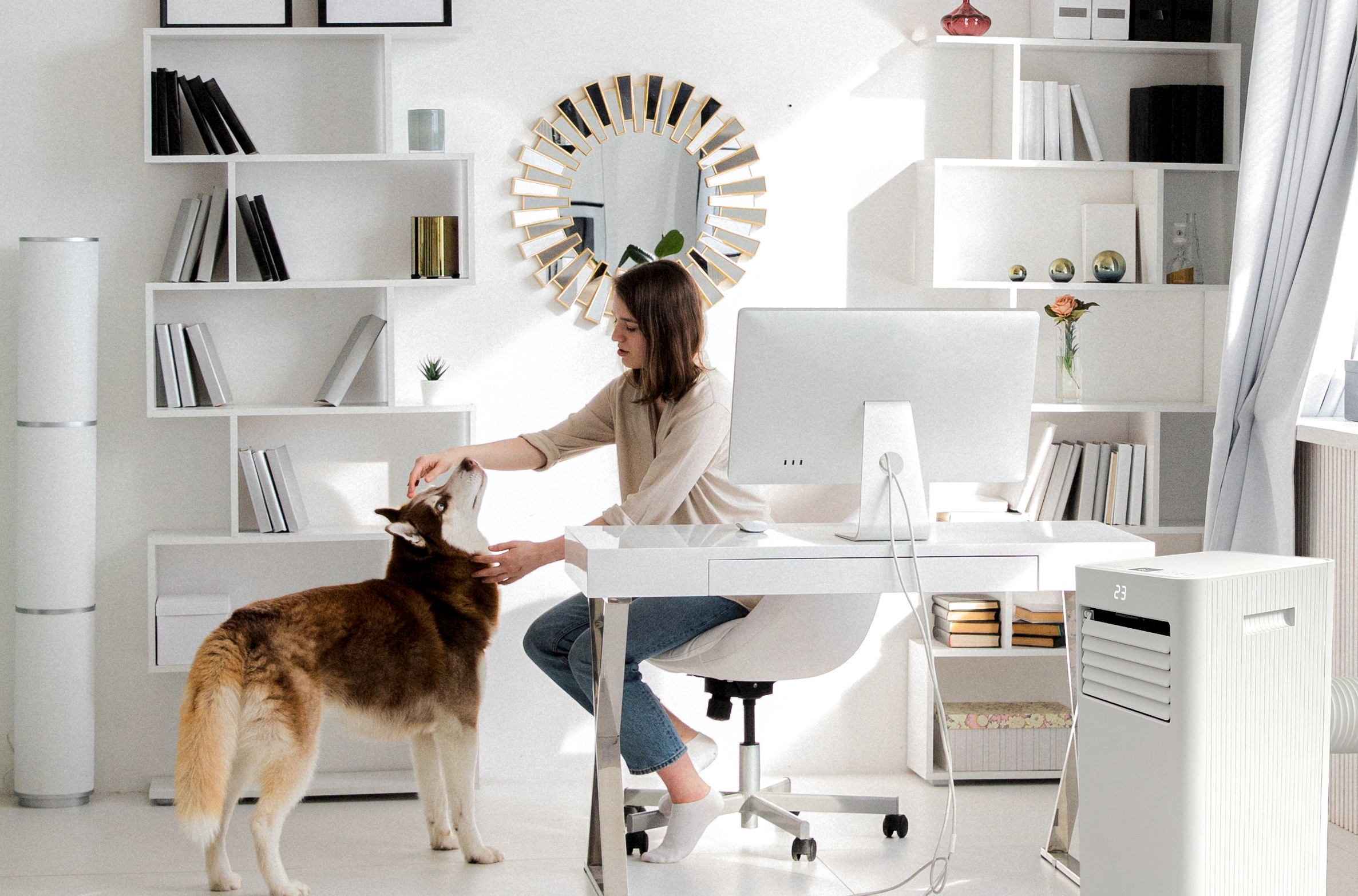 Kobieta głaszcze psa rasy husky przy biurku z komputerem.