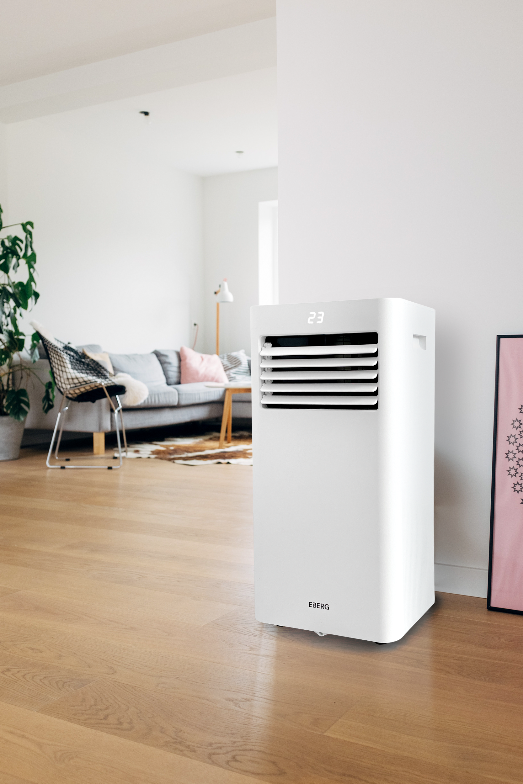 Biała przenośna klimatyzacja stoi na drewnianej podłodze obok sofy.