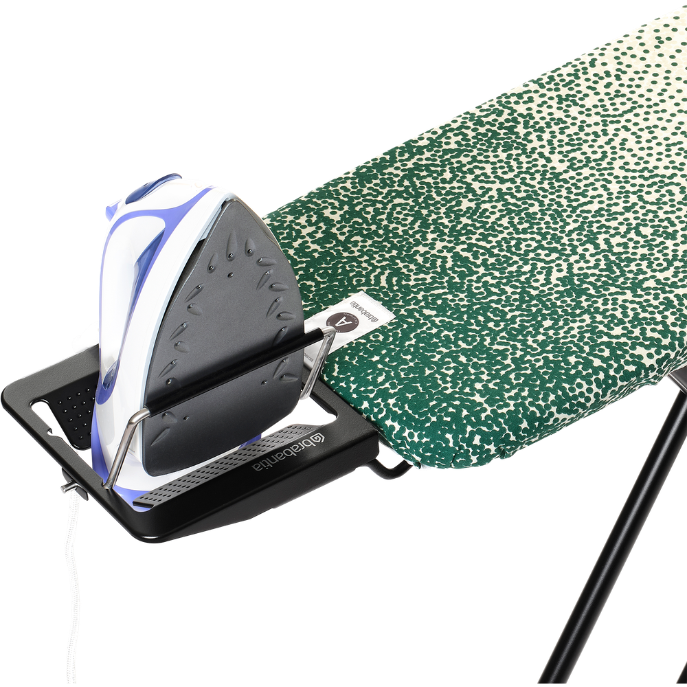 A steam iron rests on an ironing board with a green dot pattern.