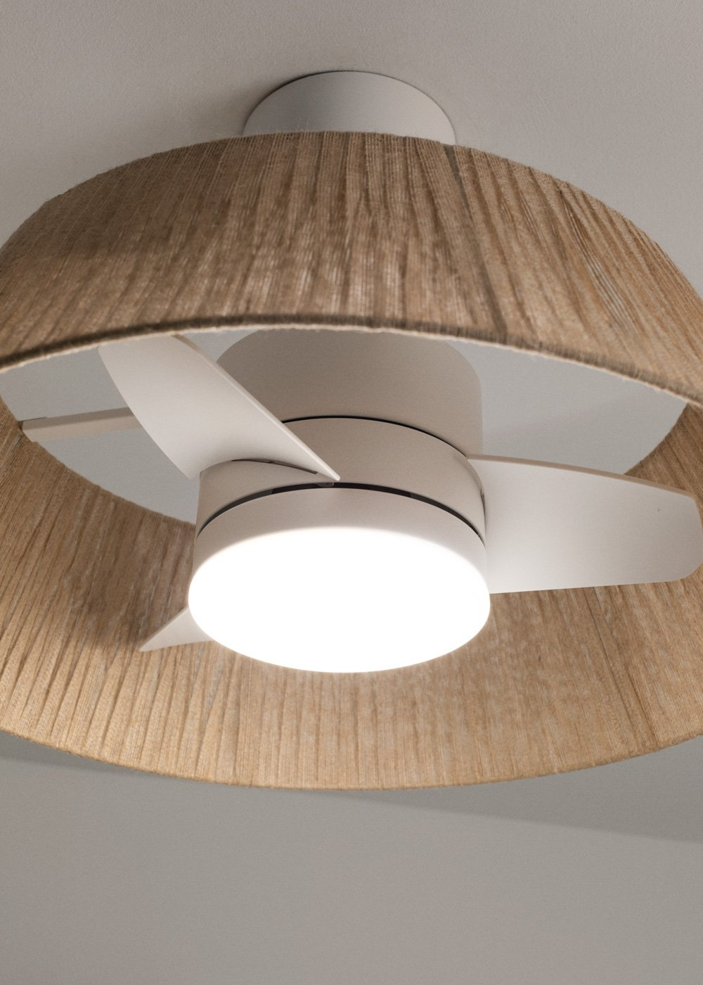 Un ventilador de techo blanco con luz, dentro de una pantalla de lámpara beige texturizada.