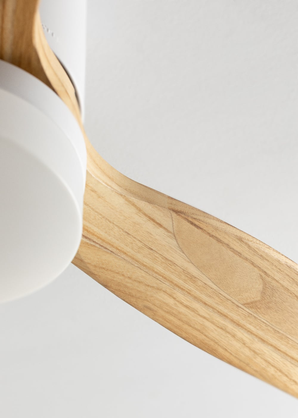 Una lámpara blanca y una pala de ventilador de madera sobre fondo blanco.