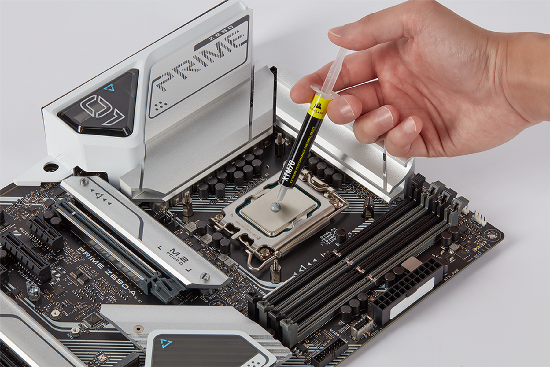 Eine Hand drückt Wärmeleitpaste auf eine Computer-CPU auf einem Motherboard.
