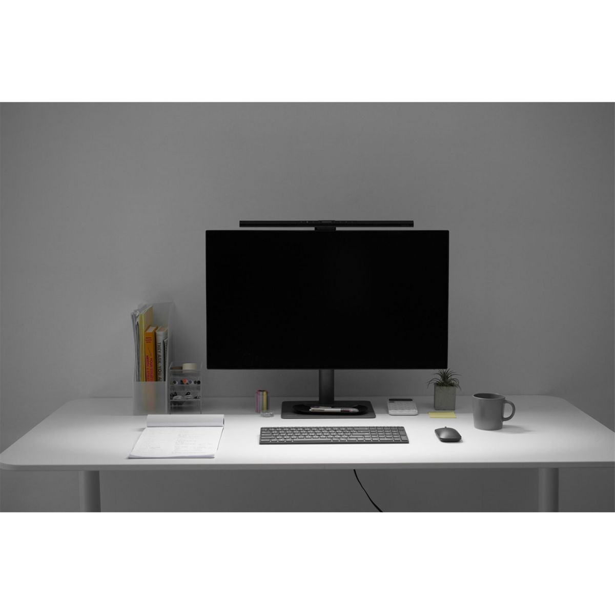 A desk with a monitor, keyboard, mouse, notepad, and mug.