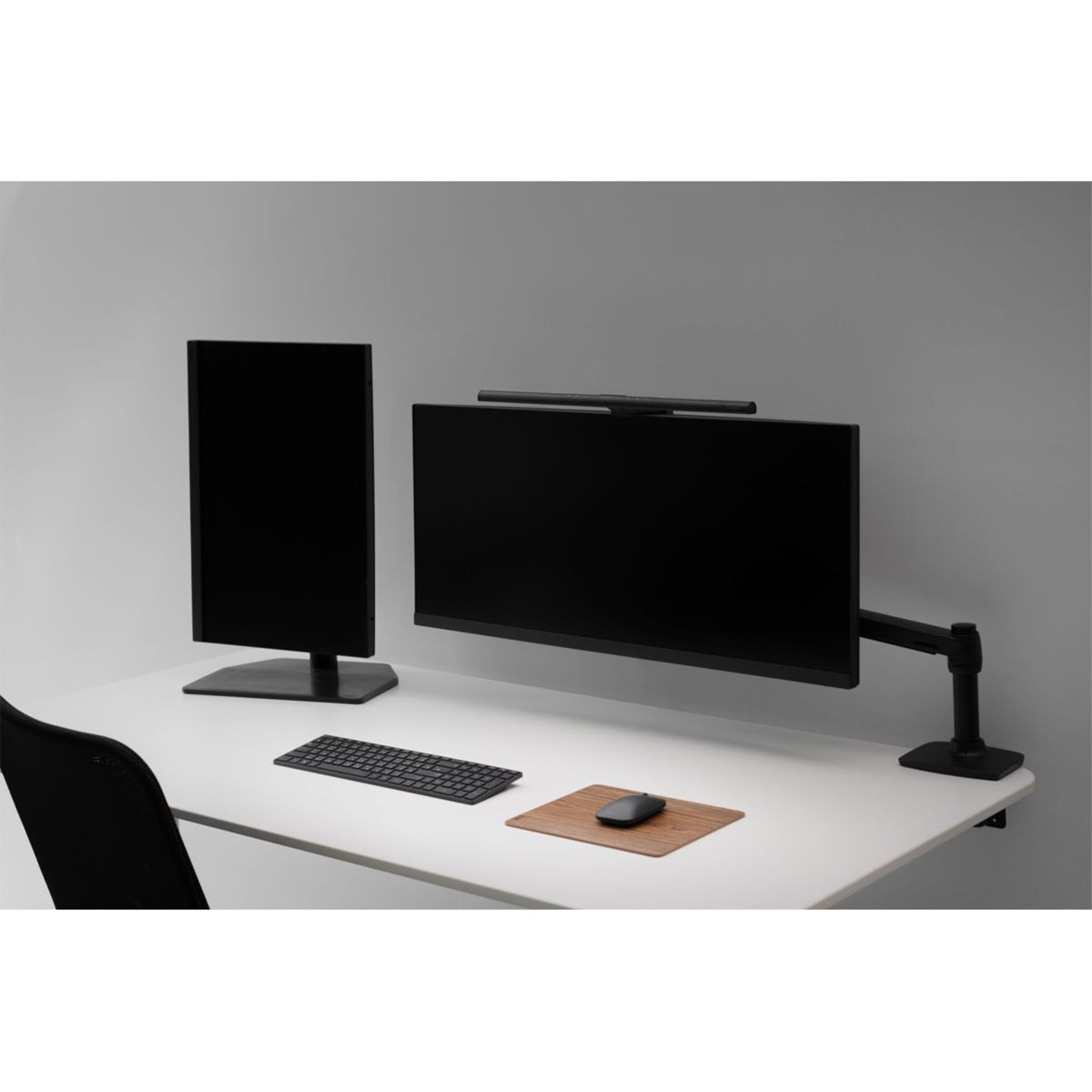 A modern desk setup with two black monitors, keyboard, mouse, and a desk lamp.
