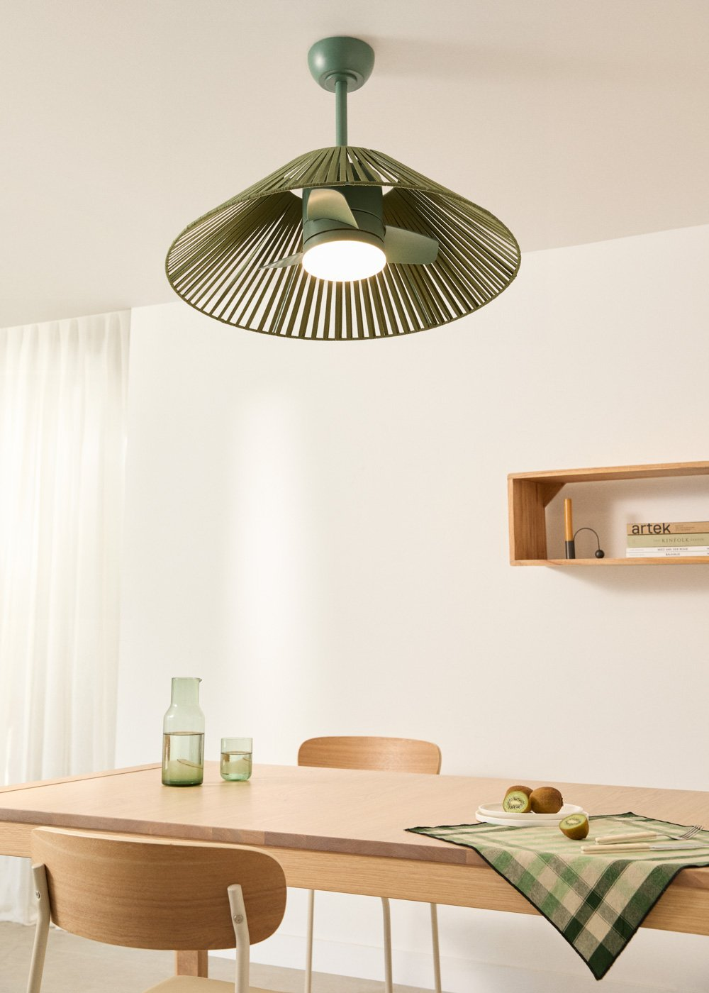 Una mesa de comedor con taburetes, jarra, vaso, fruta y ventilador de techo.