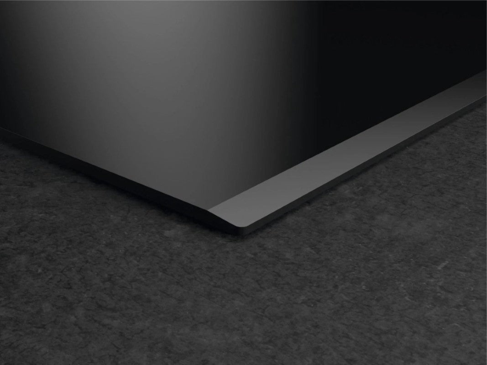 Black induction hob with grey trim on a dark stone surface.