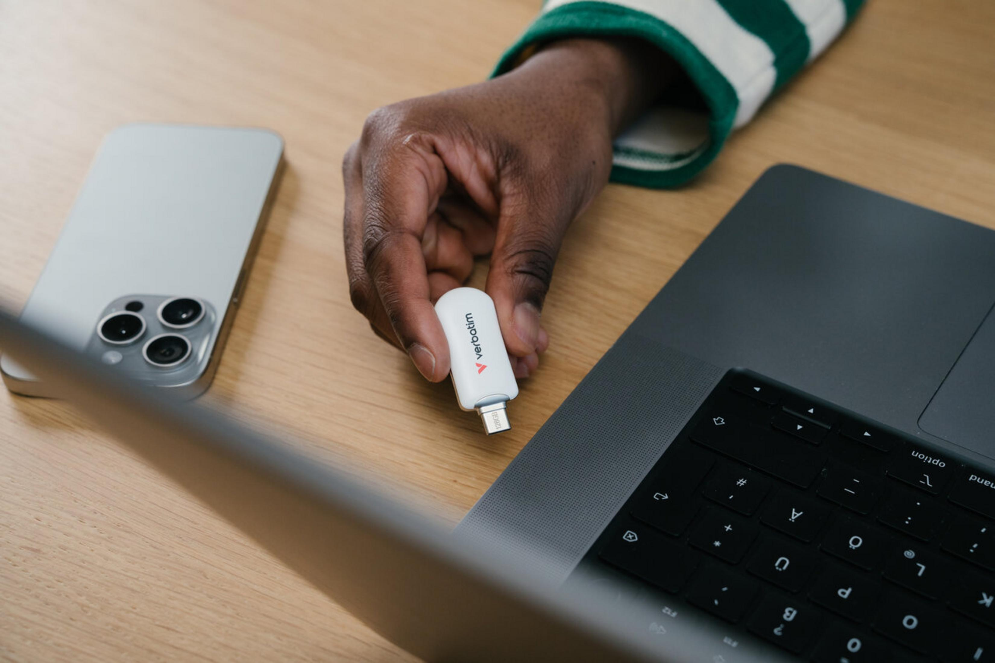 Mano tiene una chiavetta USB bianca accanto a iPhone e laptop.