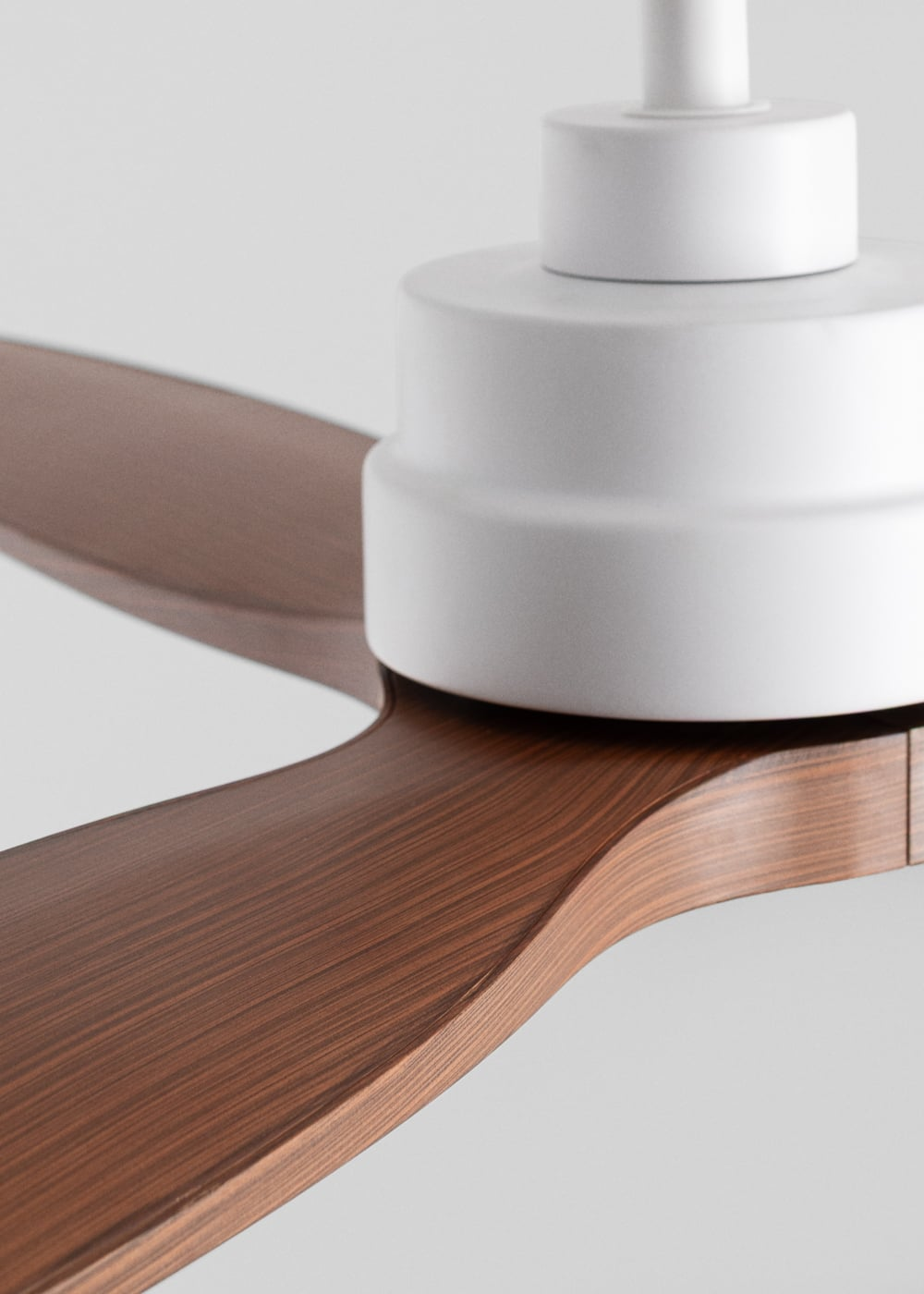 Un ventilador de techo moderno con partes blancas y aspas de madera marrón.