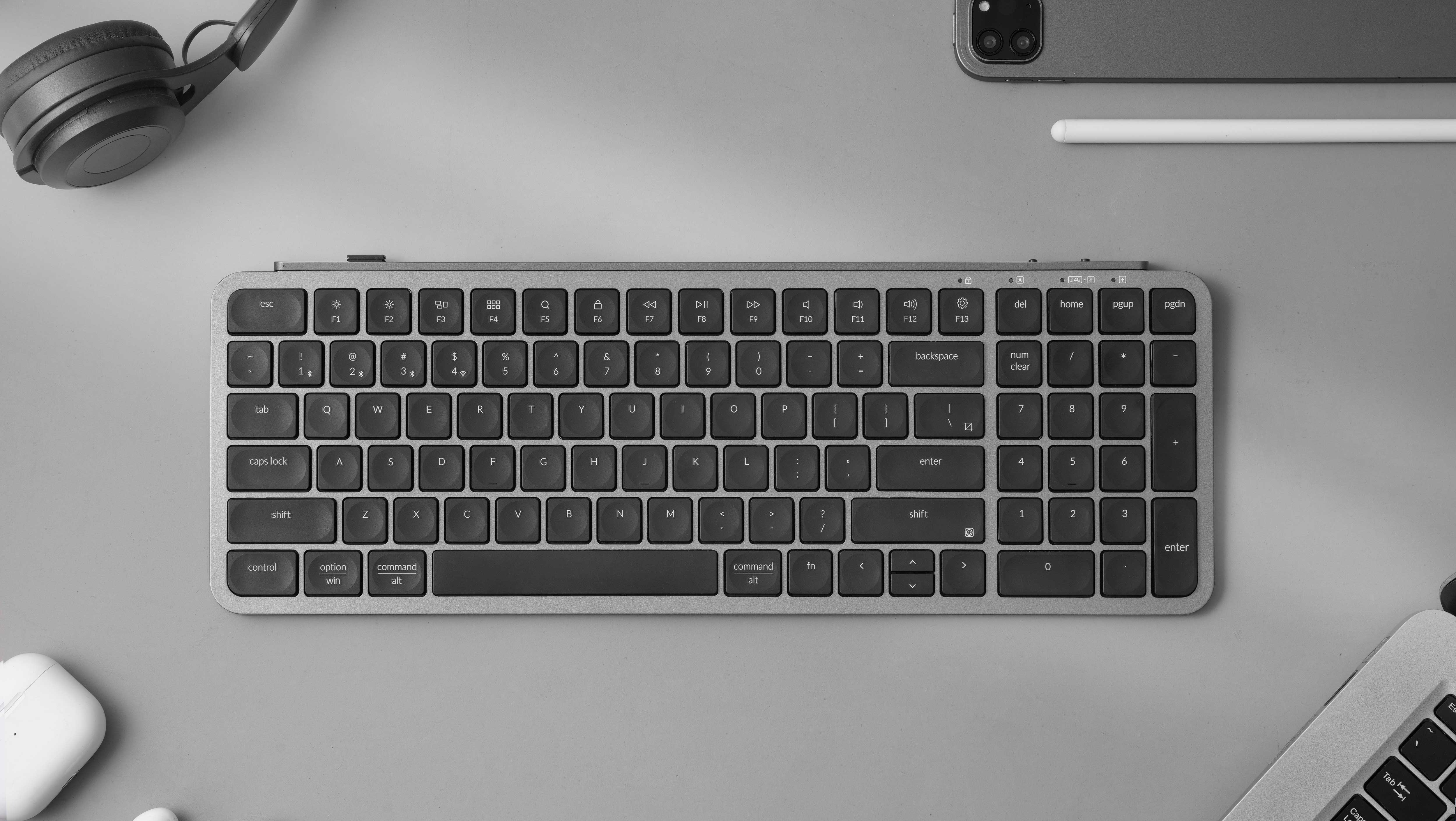 Szara klawiatura, słuchawki, tablet i rysik na szarej powierzchni.