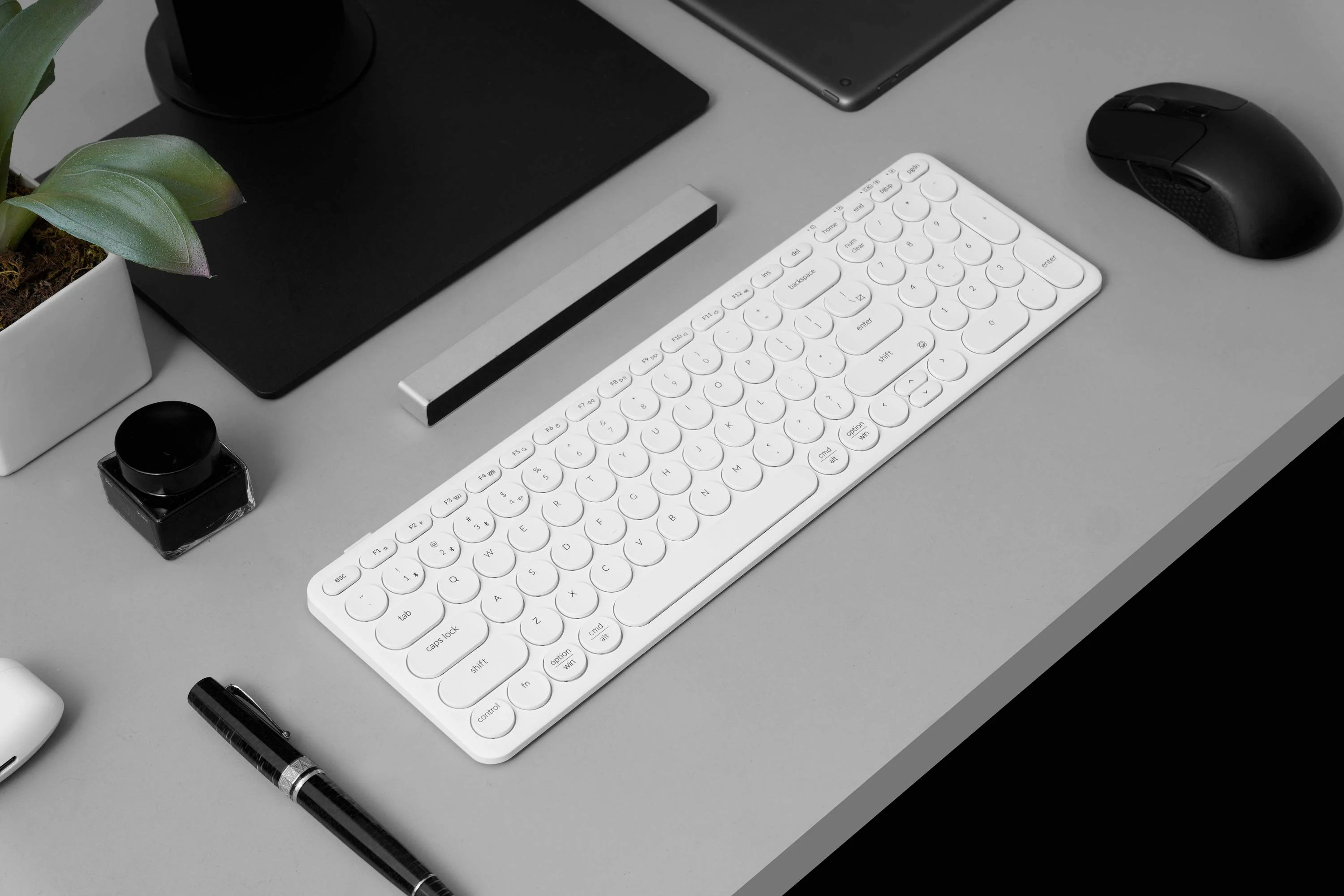 Biała klawiatura, czarna mysz i notatnik na biurku.