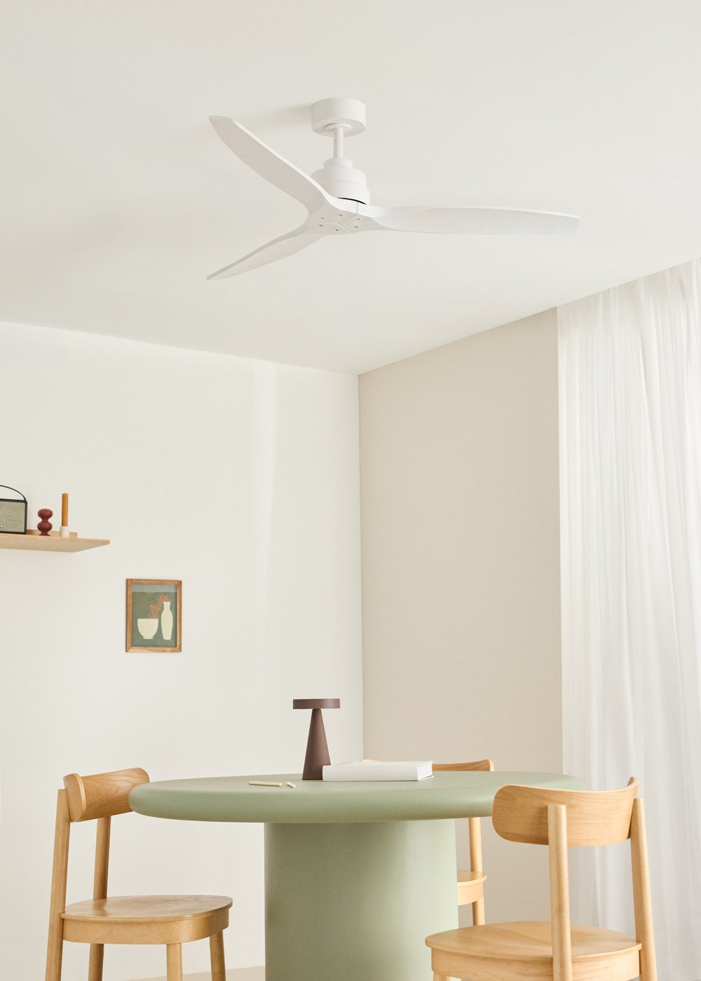 Un ventilador de techo blanco sobre una mesa redonda verde pálido con sillas de madera. Un cuadro pequeño en la pared.
