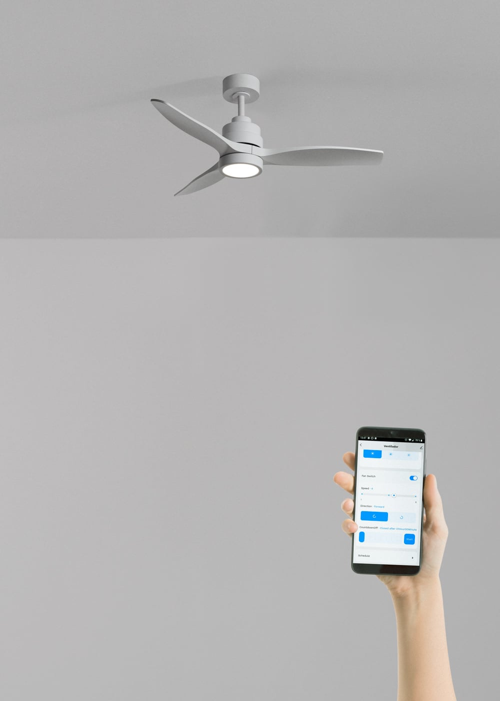 Un ventilador de techo gris con luz es controlado por una mano con un smartphone.