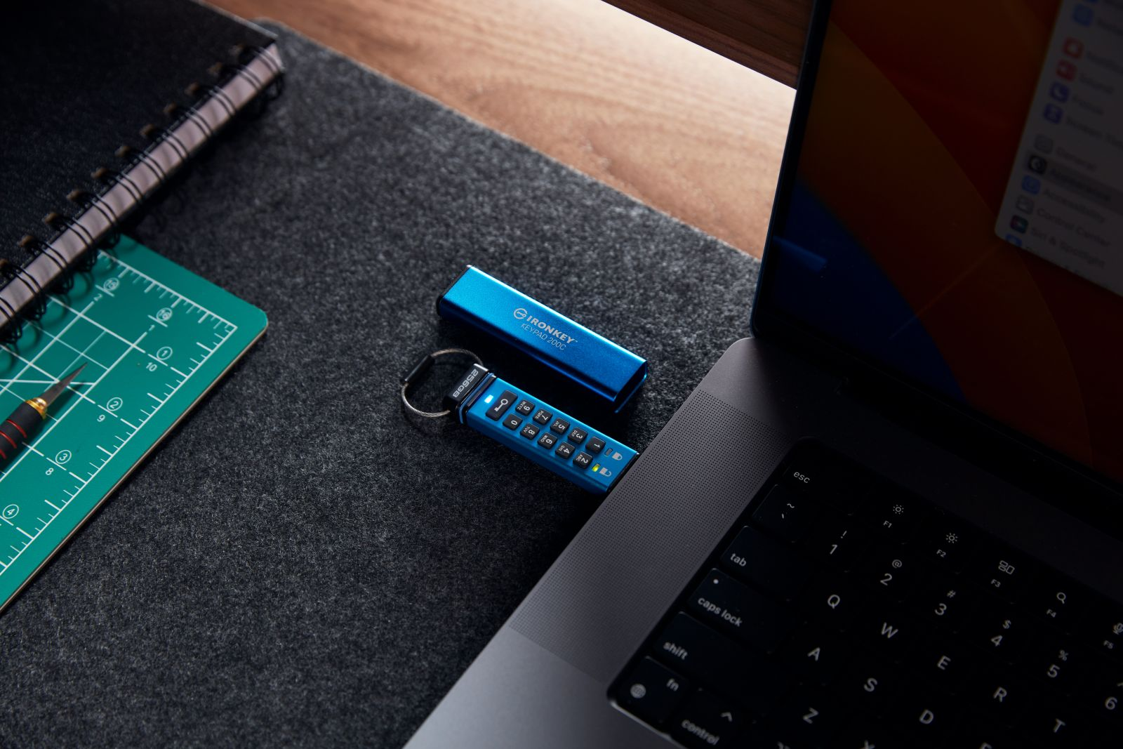 Blauer IronKey USB-Stick mit Tastatur auf einer Laptop-Tastatur, neben einem Notizbuch.