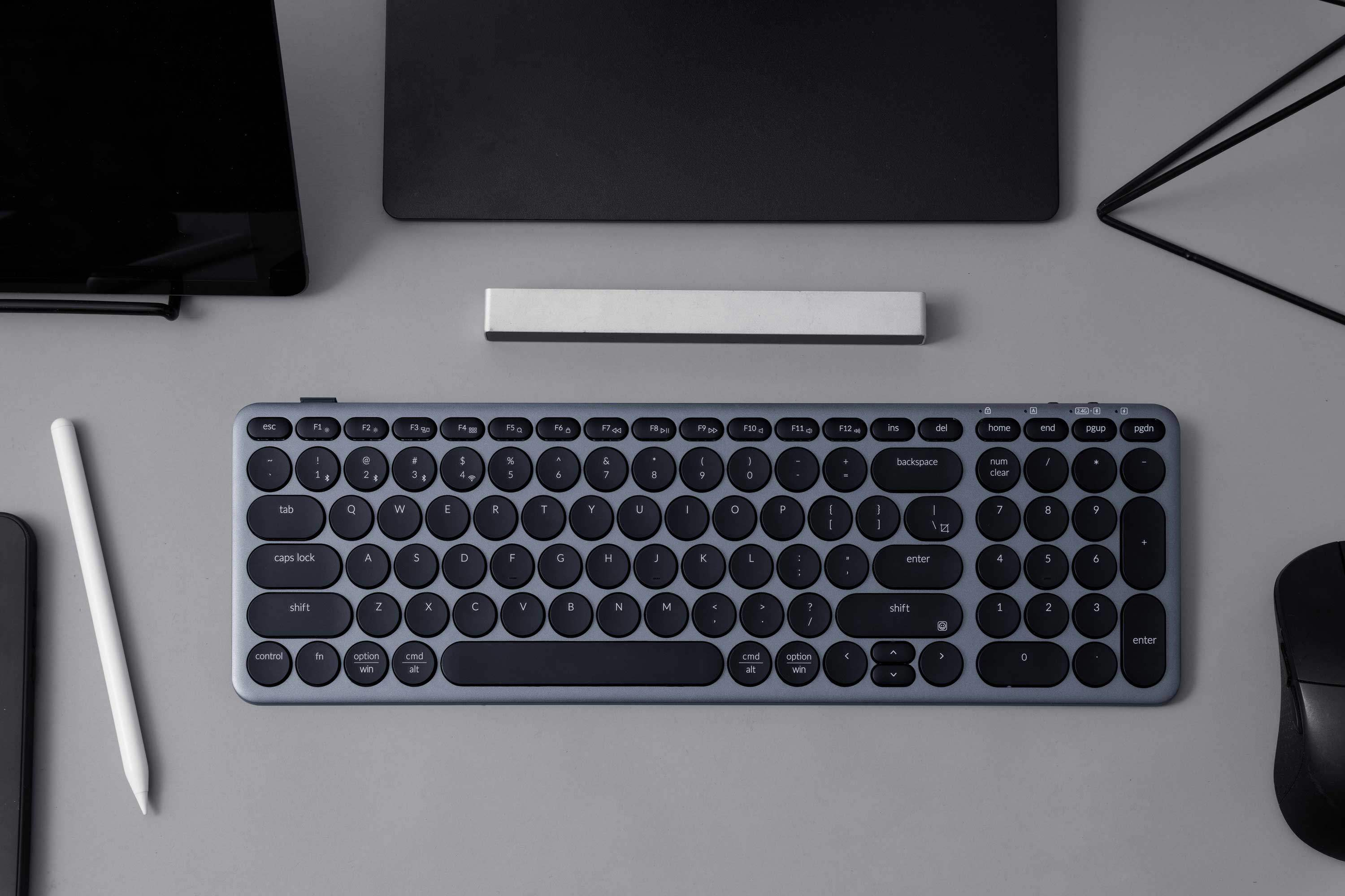 Szara klawiatura, długopis i mysz na szarym stole.