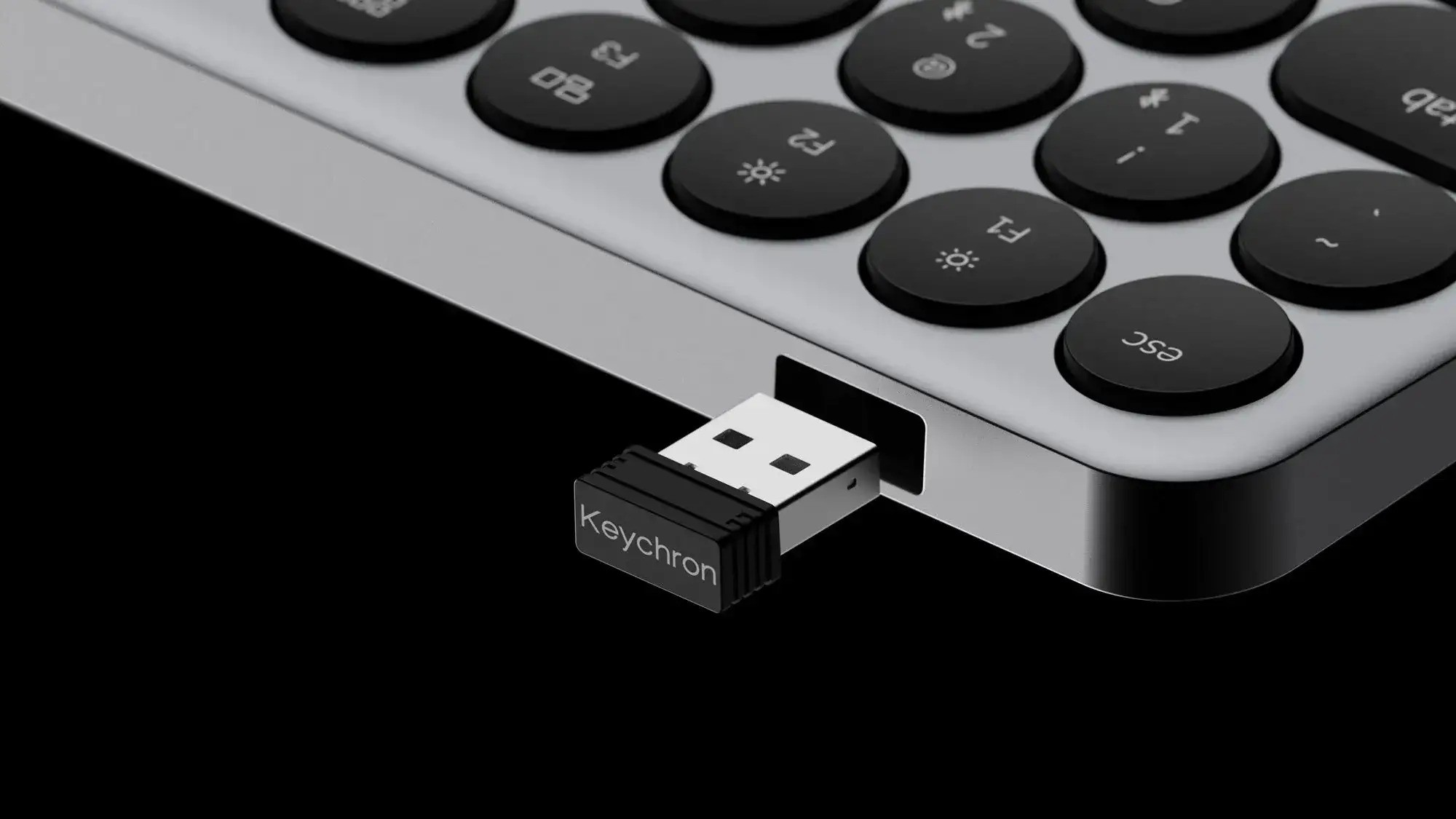 Klucz USB Keychron jest podłączony do srebrnej klawiatury na czarnym tle.