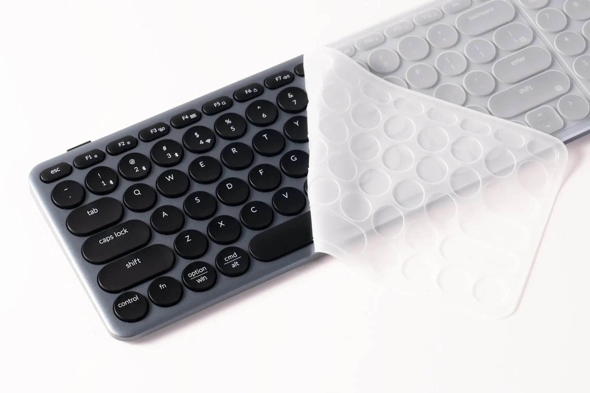 Szara klawiatura z przezroczystą osłoną ochronną częściowo podniesioną.