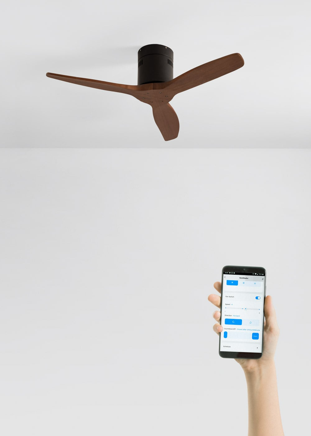 Una mano sostiene un smartphone con una app de control de ventilador sobre un ventilador de techo de aspas de madera.
