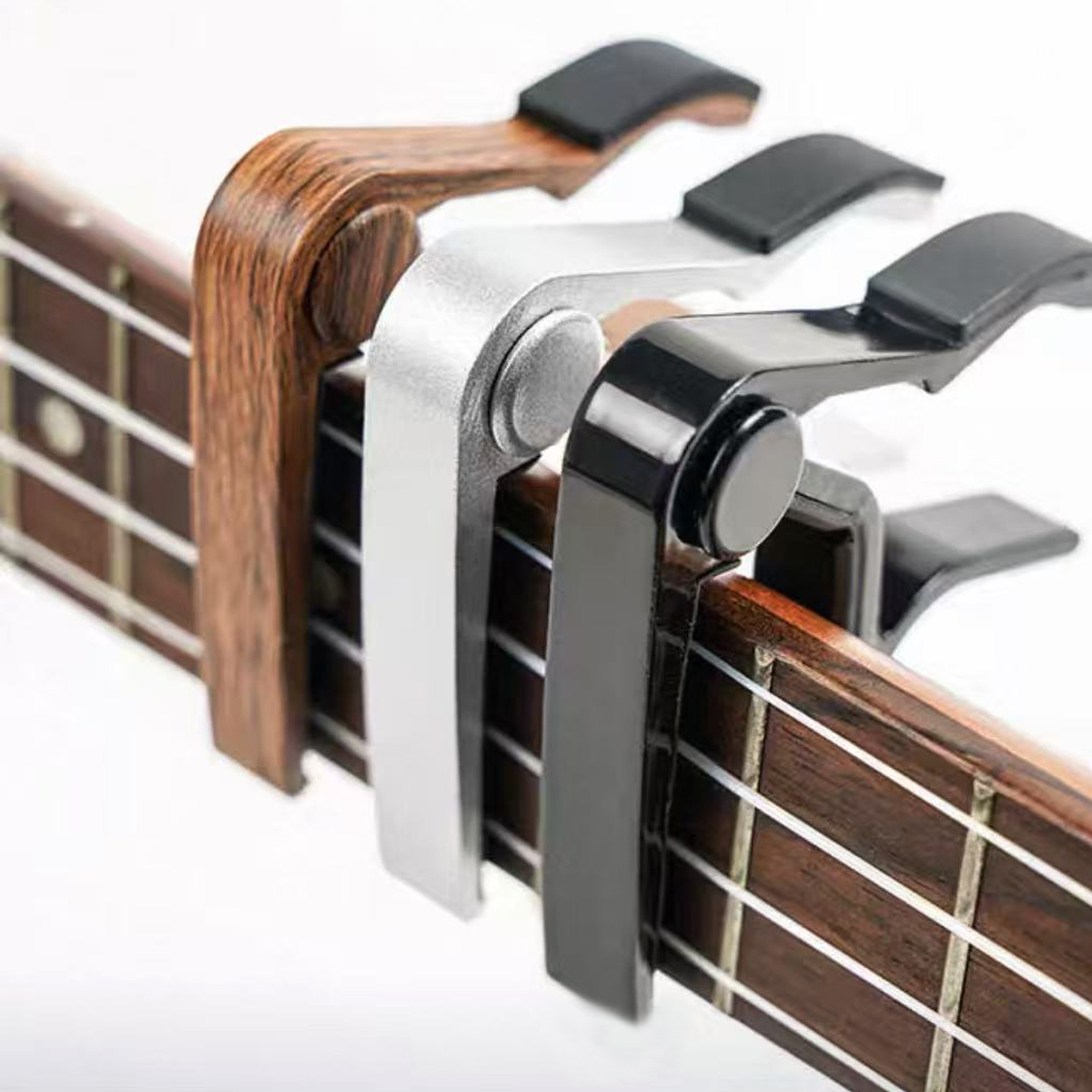 Tres capos de guitarra en madera, plata y negro en un diapasón.