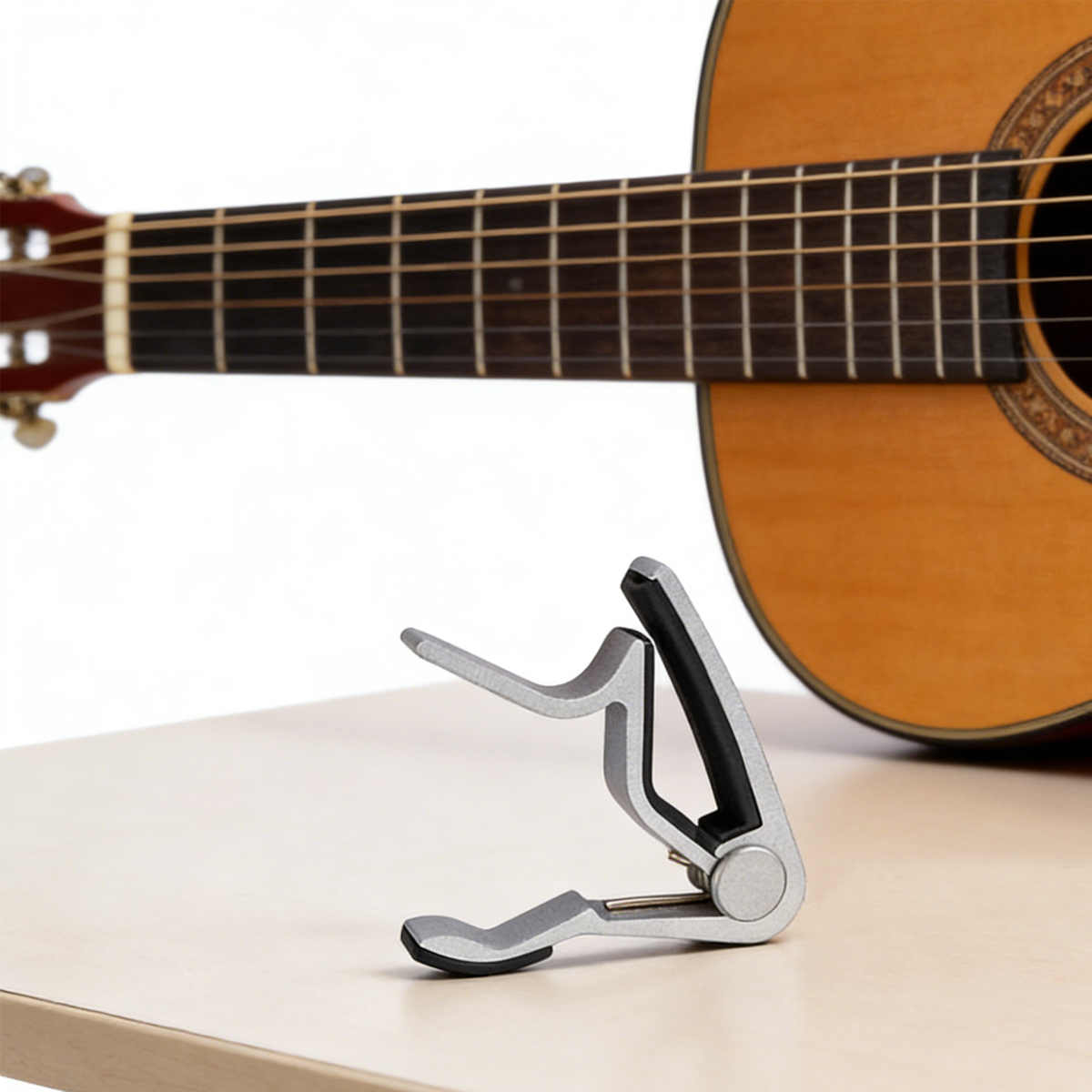 Capodastro plateado sobre mesa de madera con guitarra de fondo.