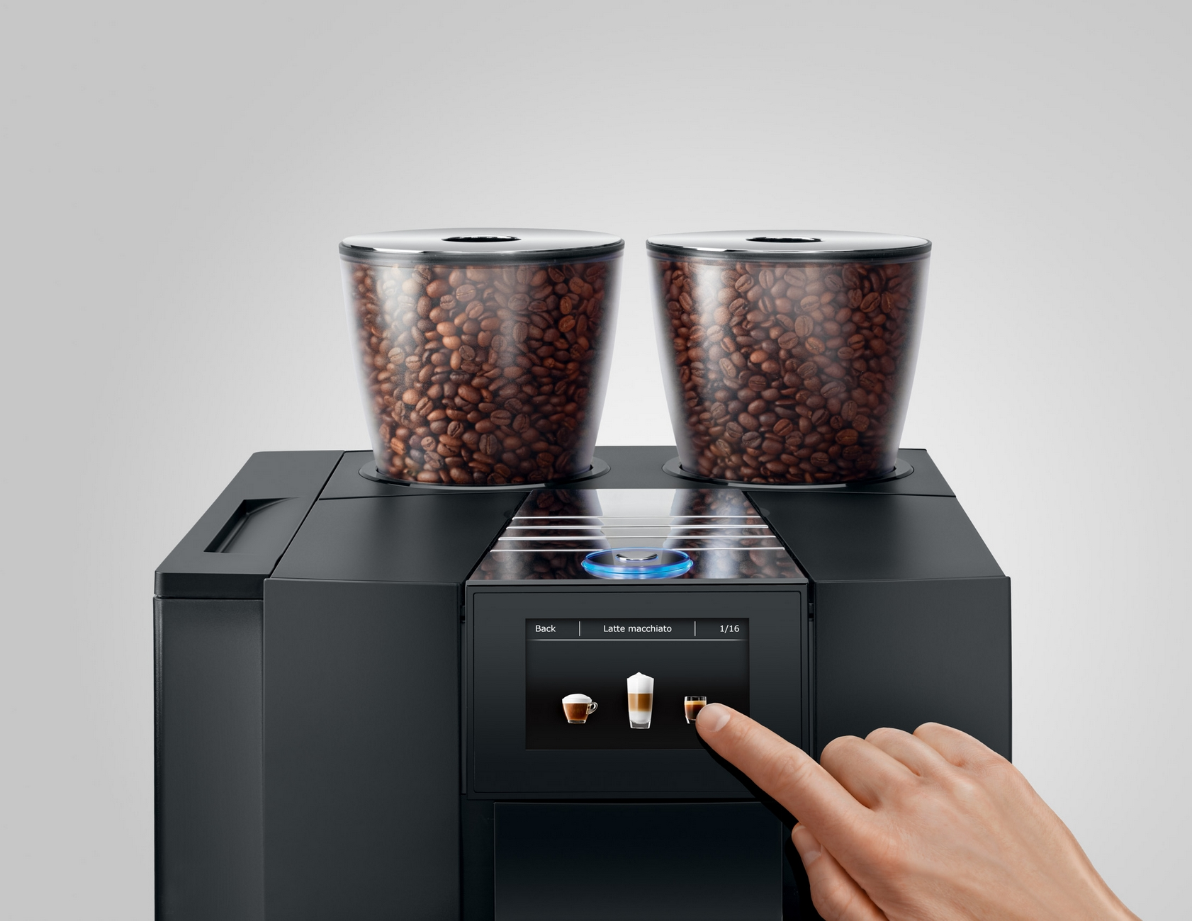 Una macchina da caffè nera con due contenitori per chicchi, un dito tocca lo schermo.