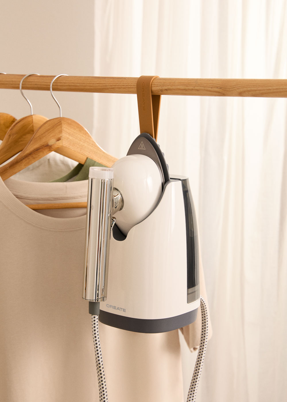 Un vaporizador de ropa blanco cuelga de una percha sobre una camiseta beige.