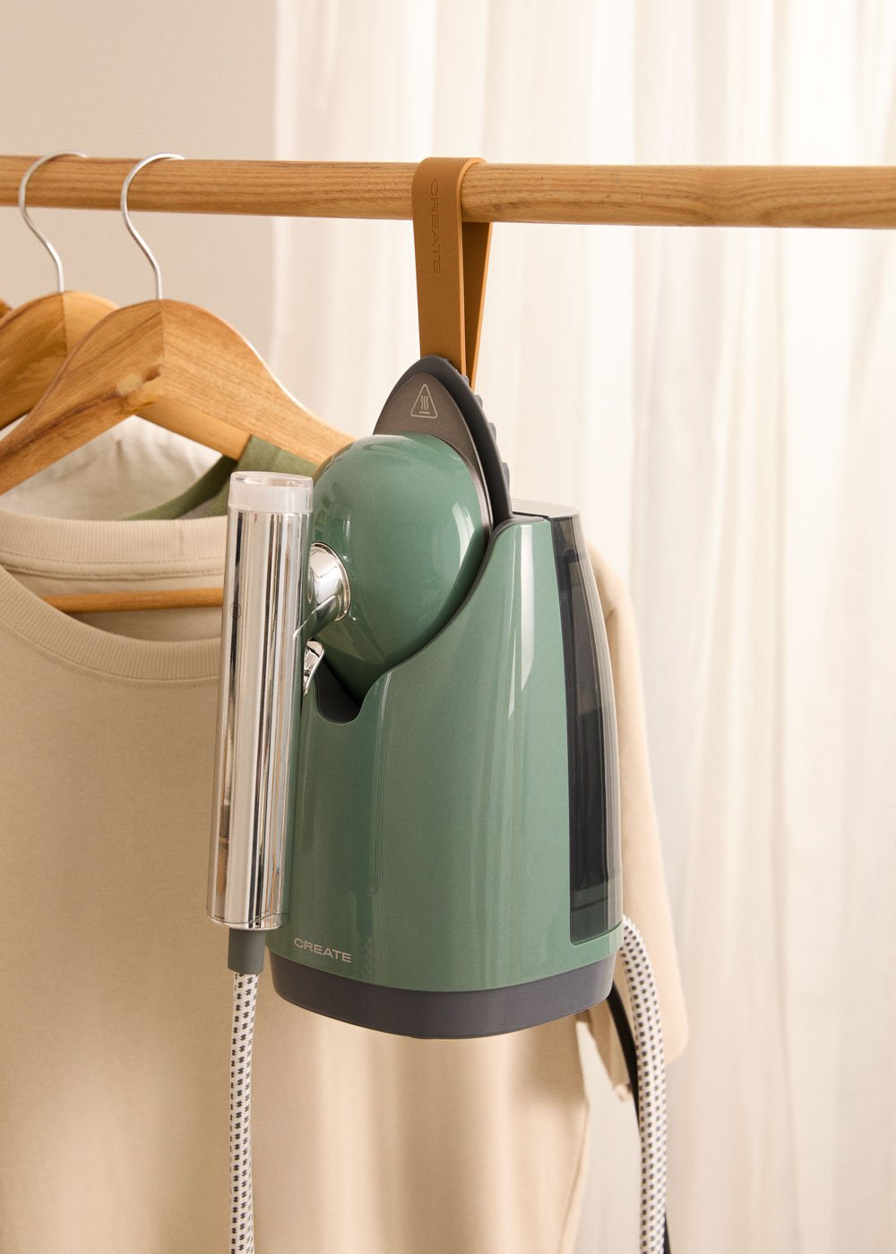 Un vaporizador de ropa verde cuelga de una barra de madera junto a ropa.