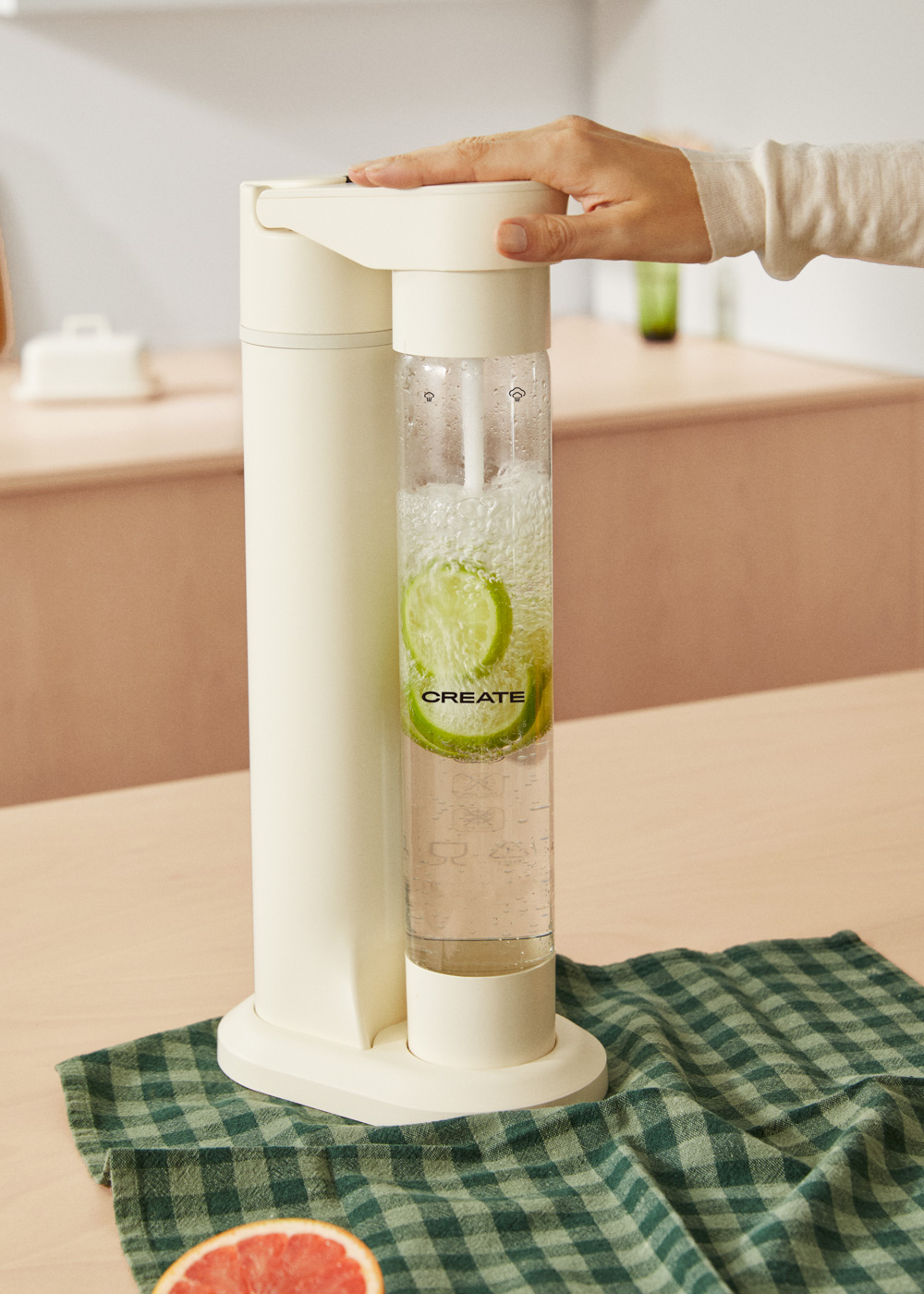 Una mano presiona un carbonatador de agua blanco con rodajas de lima en la botella.