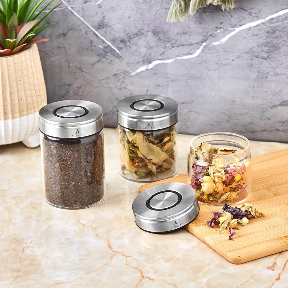 Çay veya bitki ile doldurulmuş metal kapaklı üç cam kavanoz.